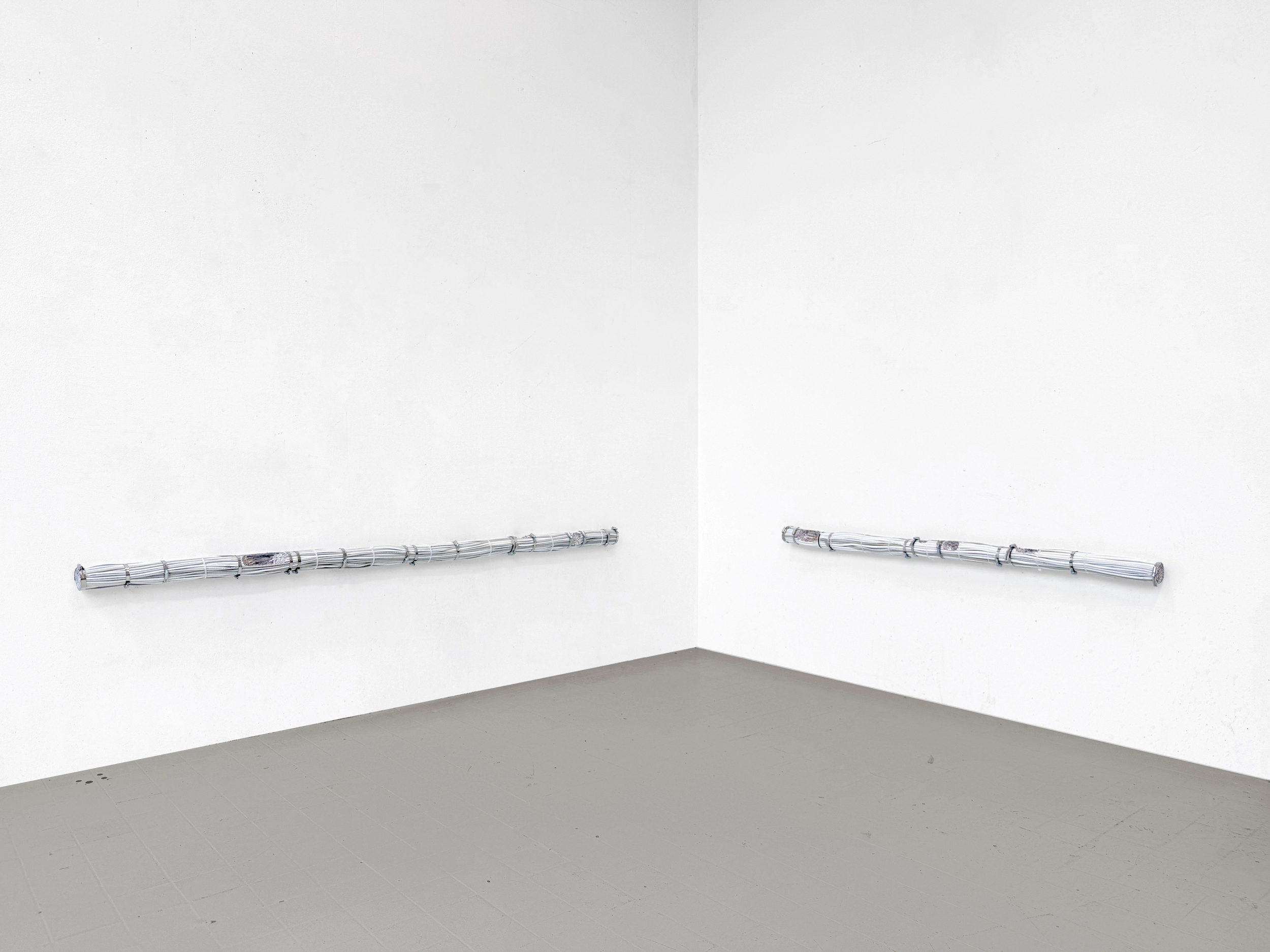 General view of Rodrigo Red Sandoval’s installation “Time Line” (2025), exhibited at Swivel Gallery in New York. Two long white cable bundles, bound with metal clamps and integrated watch elements