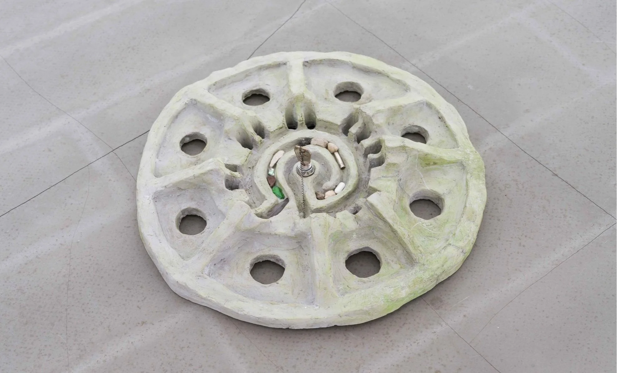 Installation view of “Group Kiss Street,” a concrete street fragment embedded with stones, debris, a key lock and chain, exhibited at Jack Barrett Gallery.