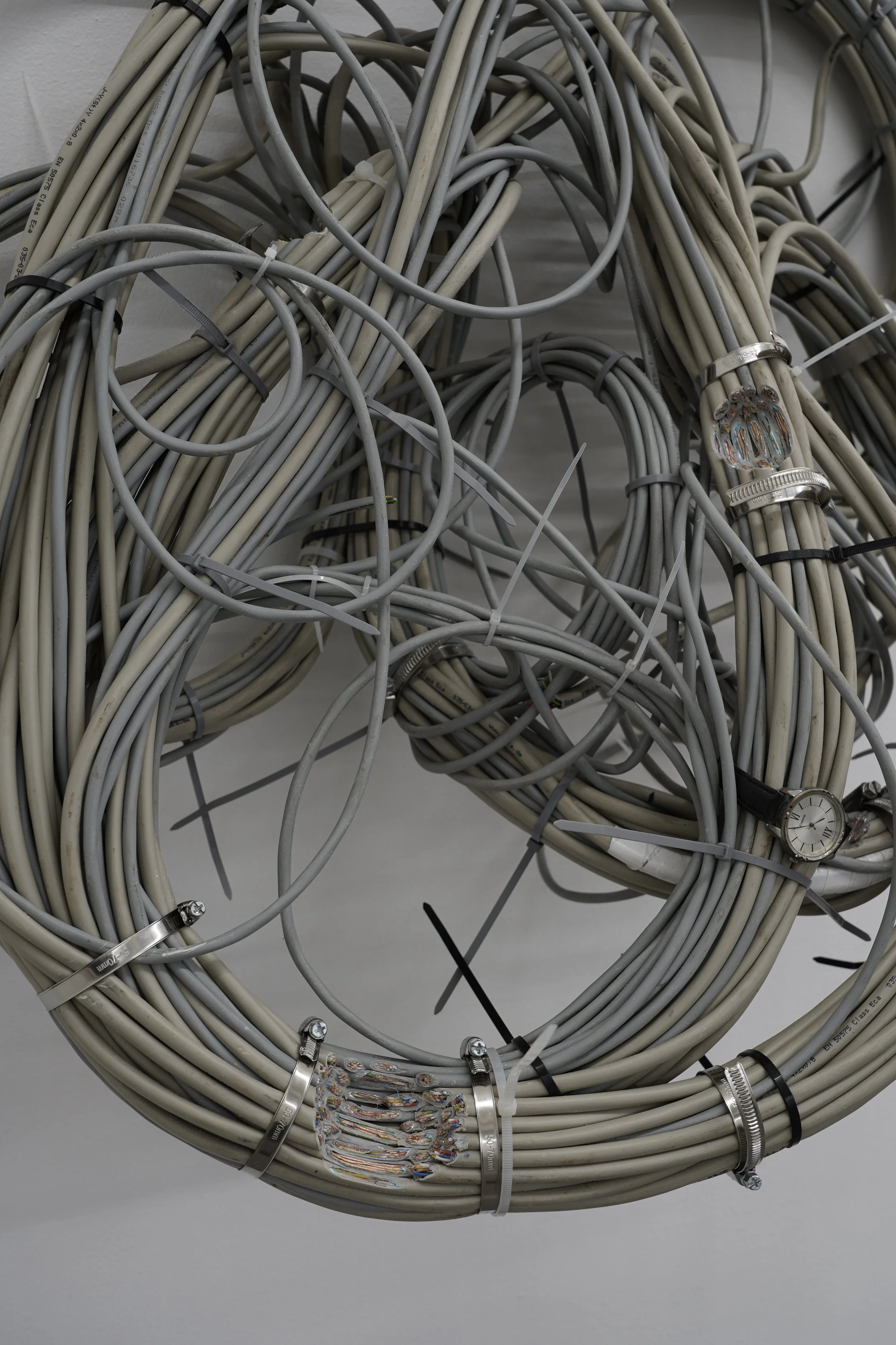 Detail of “Nest,” showing intertwined data cables, metal clamps and wrist watches forming a dense infrastructural mesh, exhibited at Platform Stockholm.