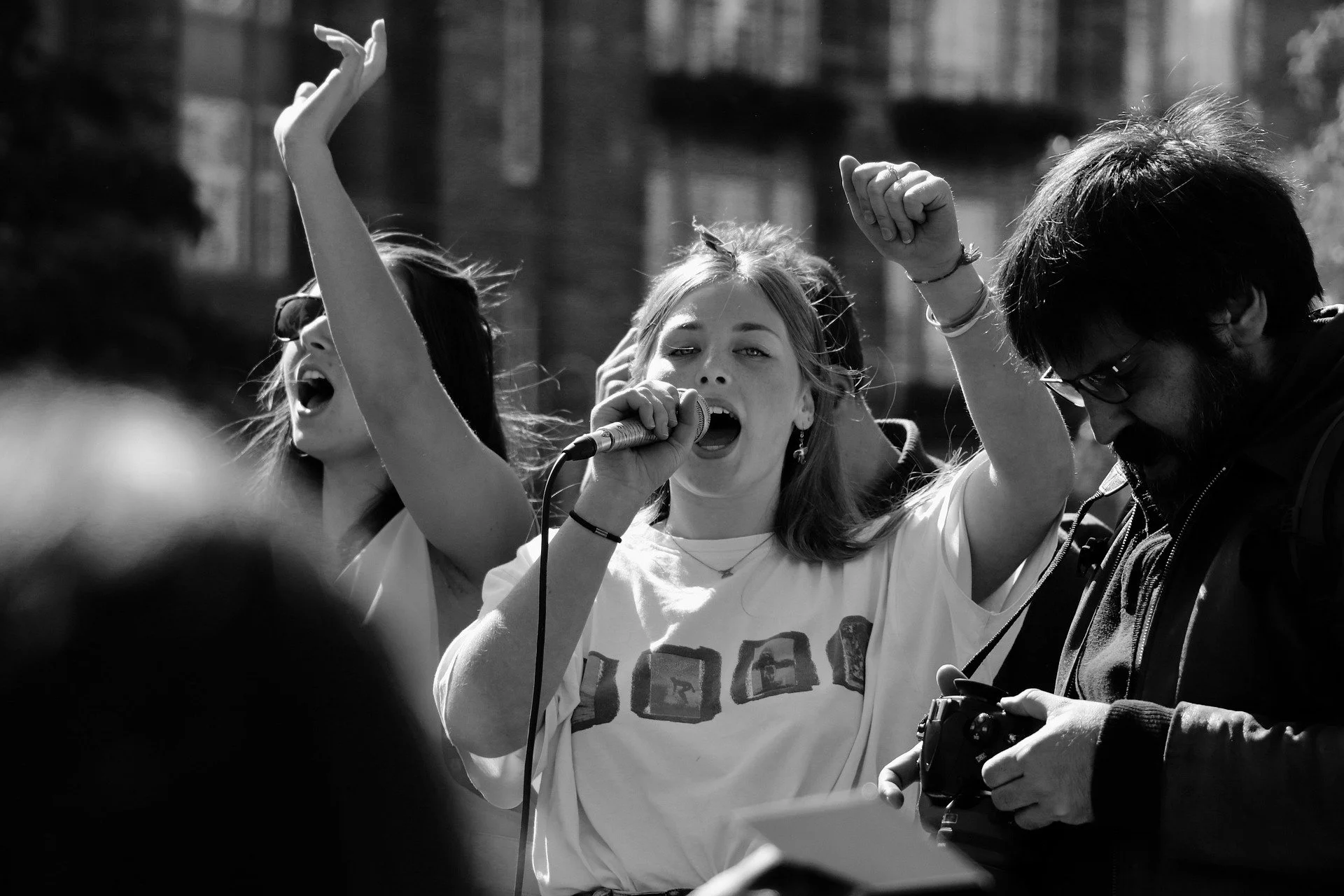 Black and white photograph of a young woman speaking into a microphone at a crowded protest