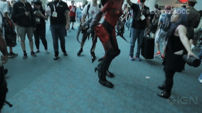 A person jumping in the air at a crowded indoor event or convention, surrounded by people watching and taking pictures.