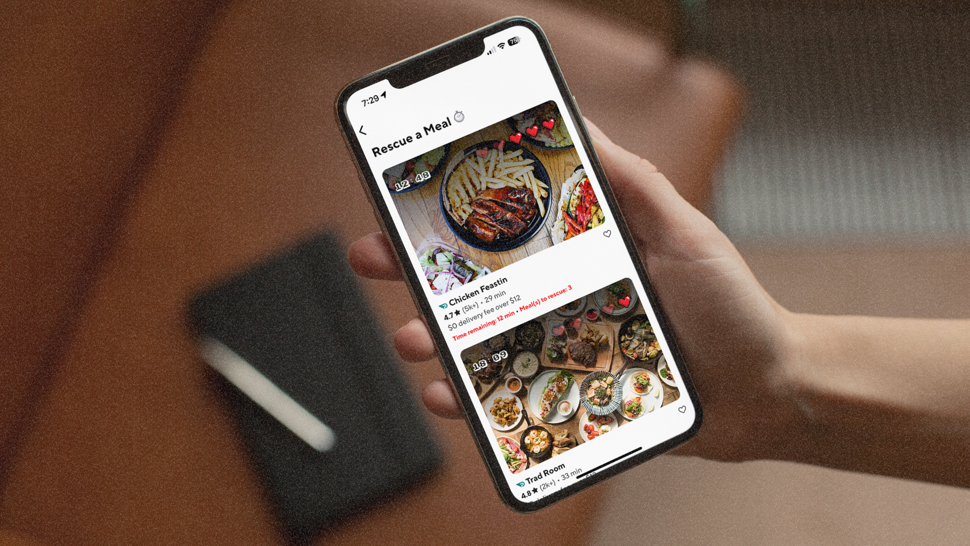 Person holding a smartphone displaying a food delivery app with images of meals, including a chicken dish with fries, salads, and assorted dishes.