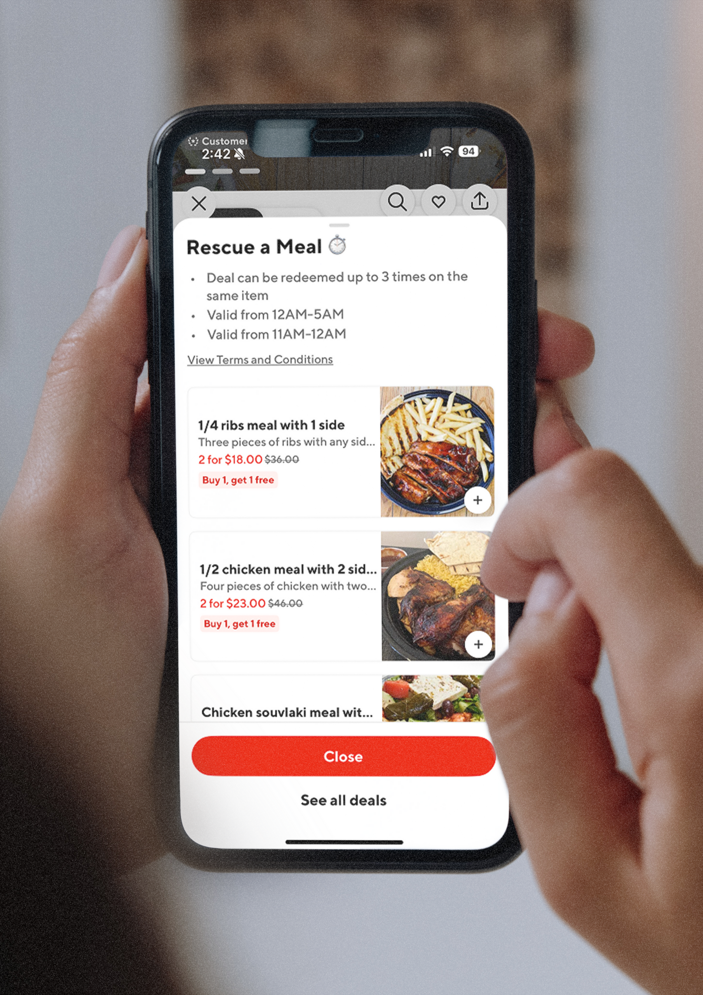Person holding a smartphone displaying a food deal app with options for ribs, chicken, and other meals.