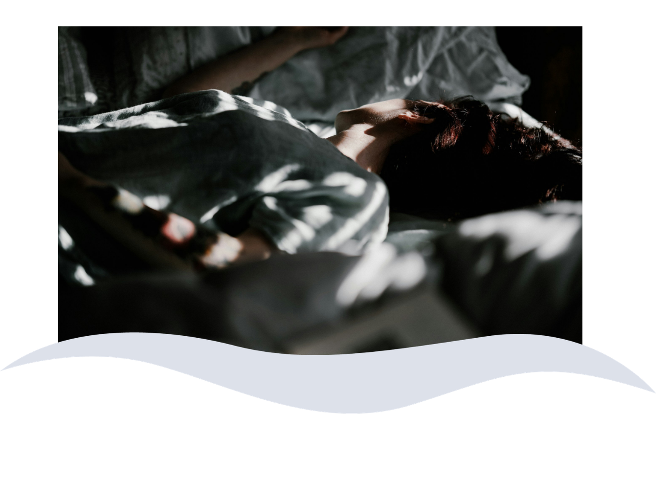 Person sleeping on a bed, partially covered with a patterned blanket, with sunlight casting shadows.