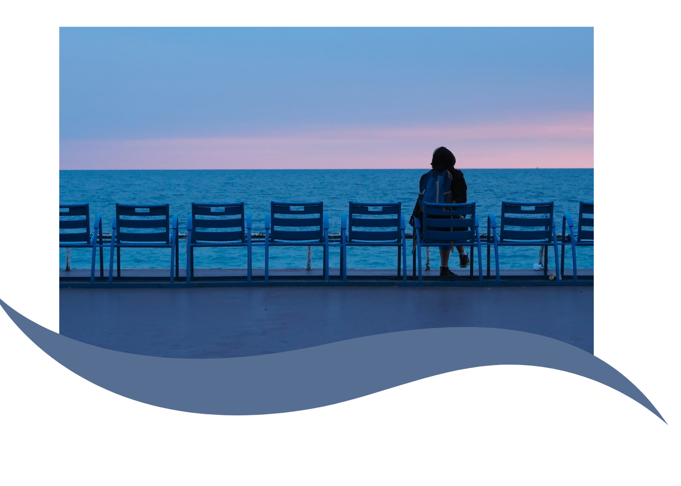 Person with backpack walking past empty chairs on a seaside promenade during sunset.