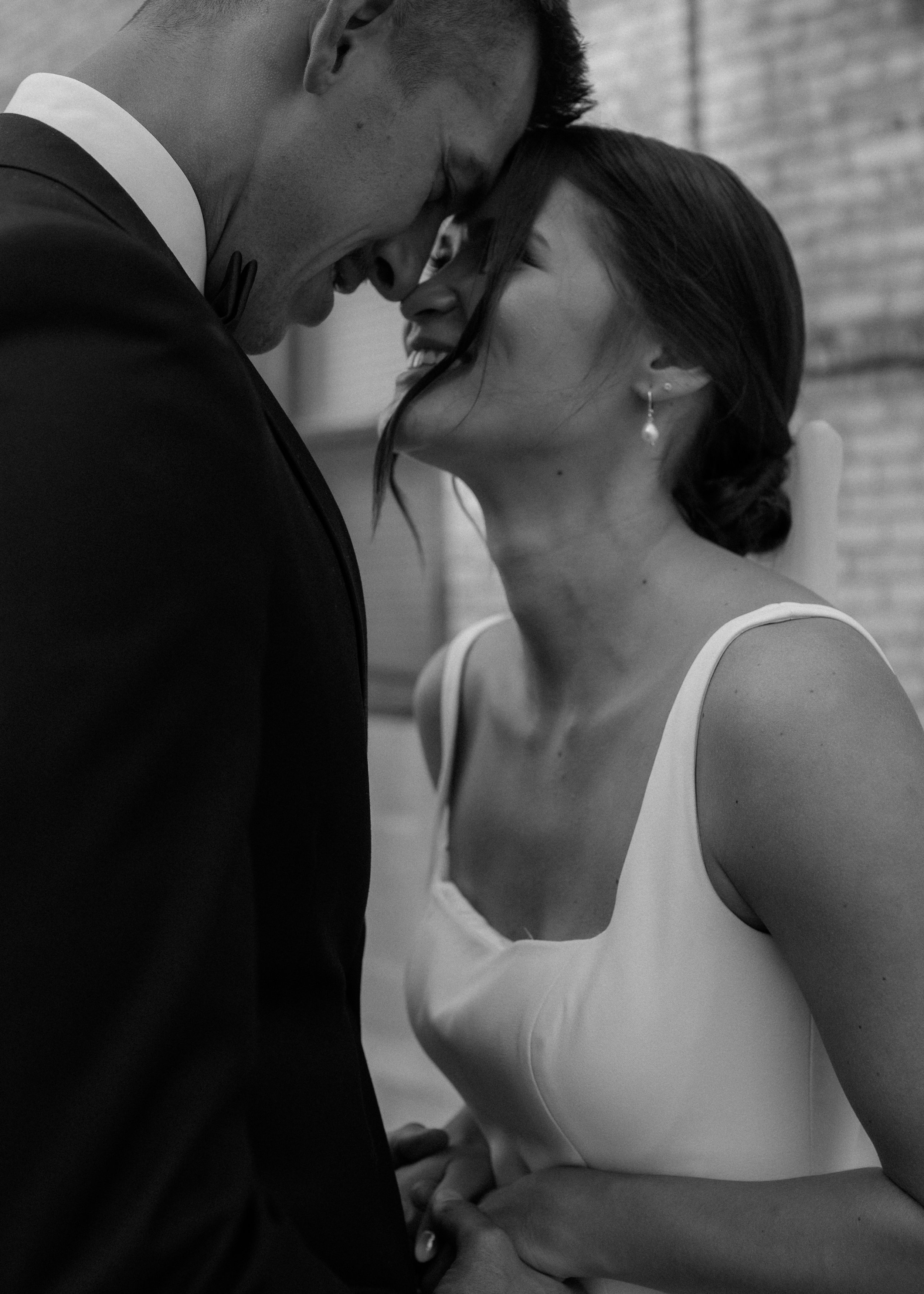 A couple dressed in formal attire sharing a tender moment, touching foreheads and smiling at each other.