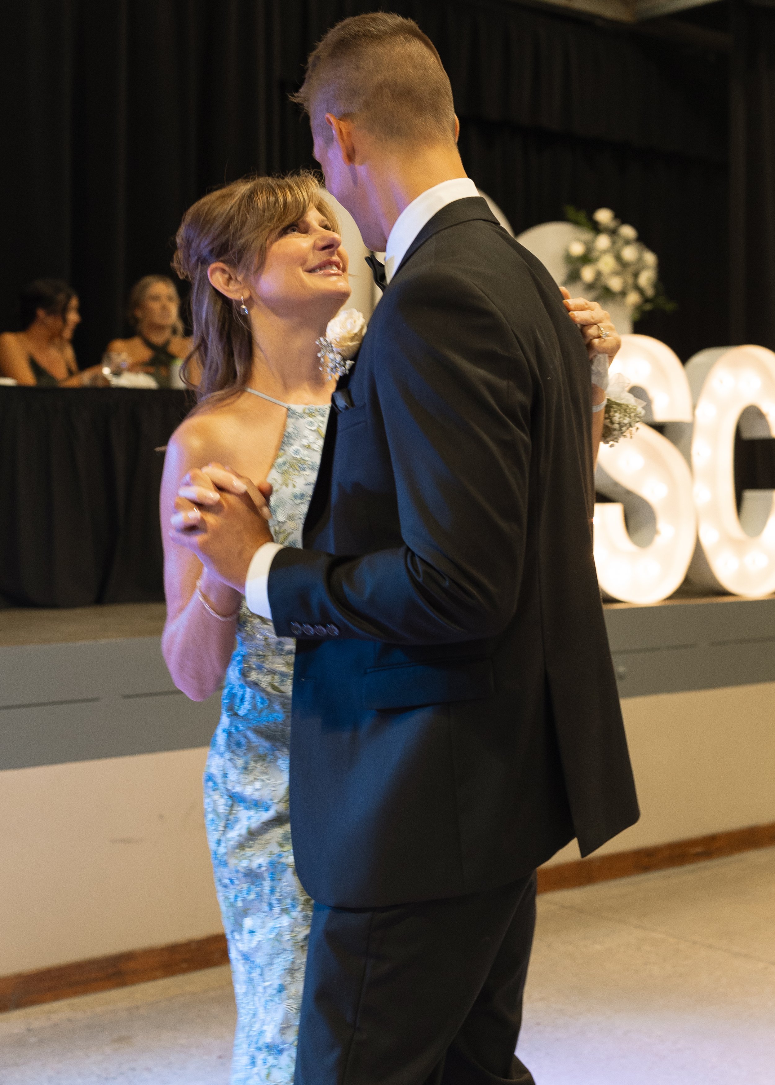A woman and a man dancing closely at a wedding celebration, with the woman smiling and looking up at the man, who is in a tuxedo.