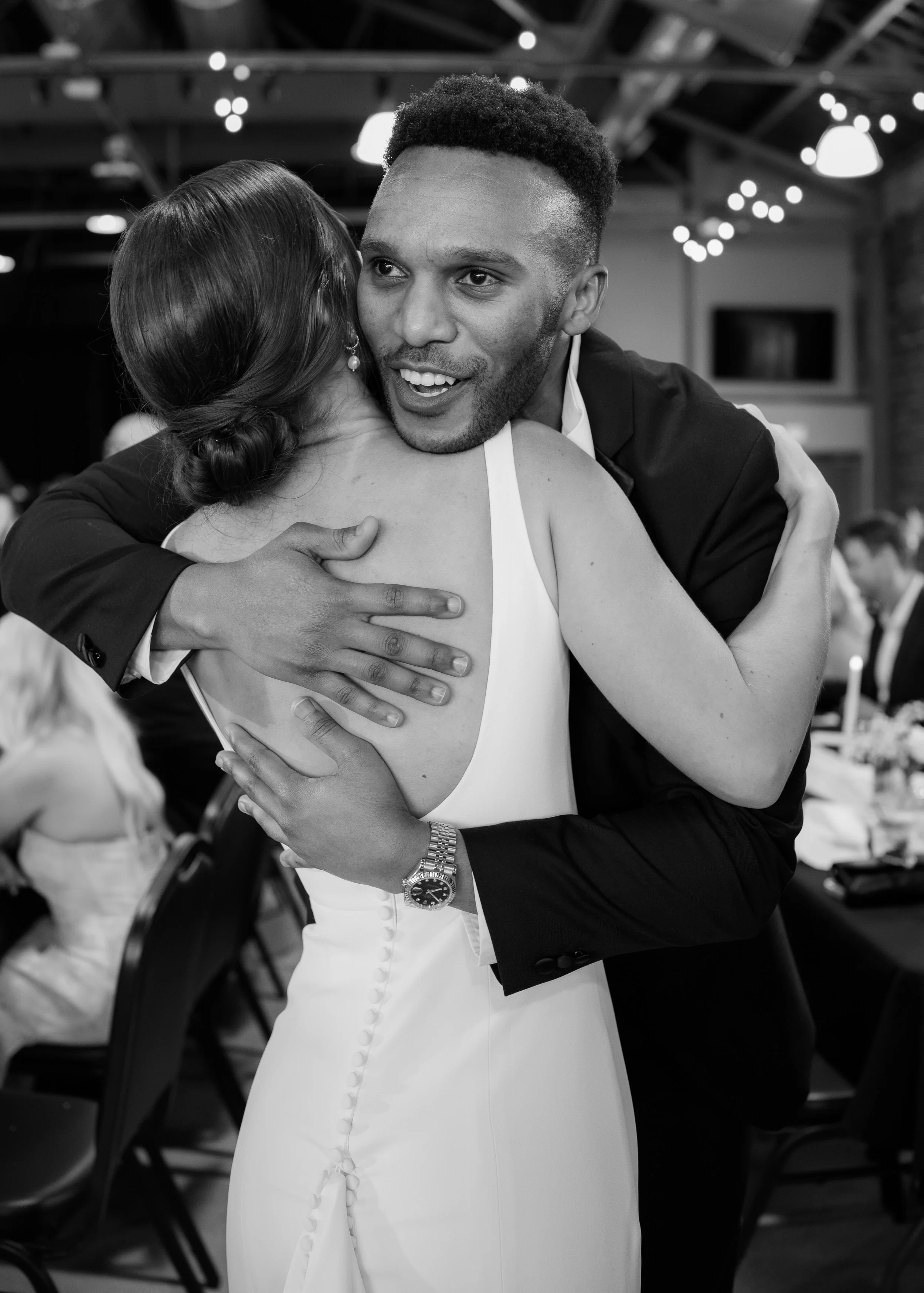 A man in a tuxedo embracing a woman in a wedding dress at a celebration event.