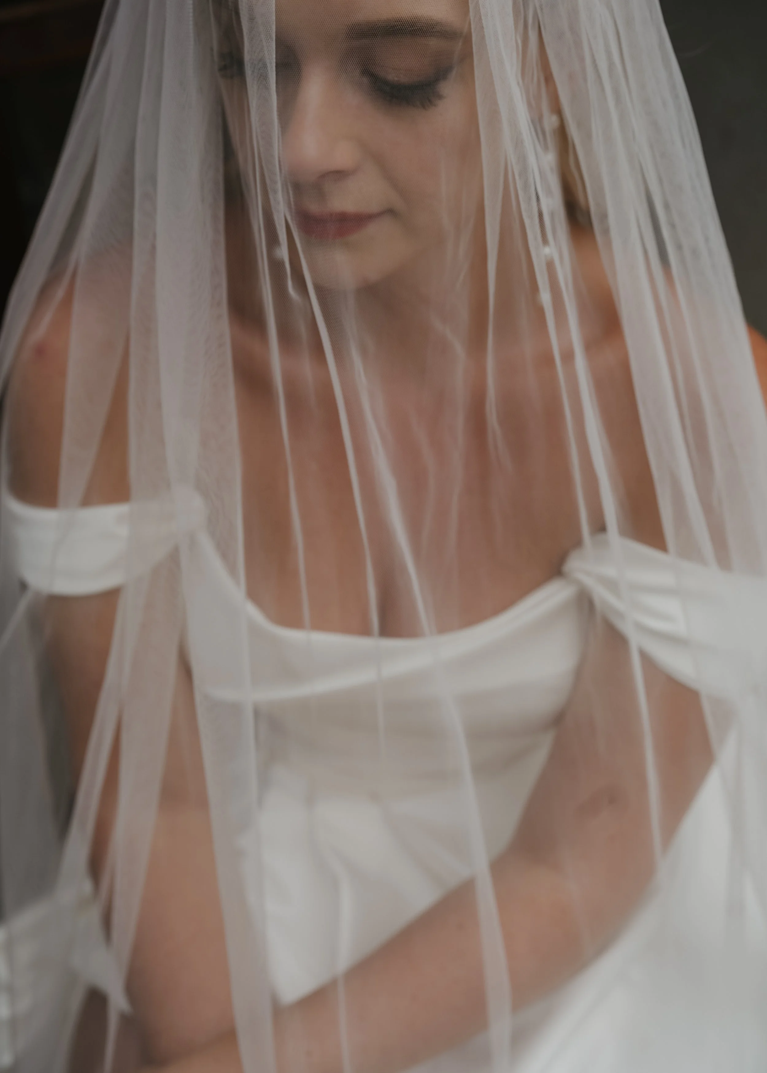 Close-up of a woman with closed eyes wearing a white dress and a sheer white veil.