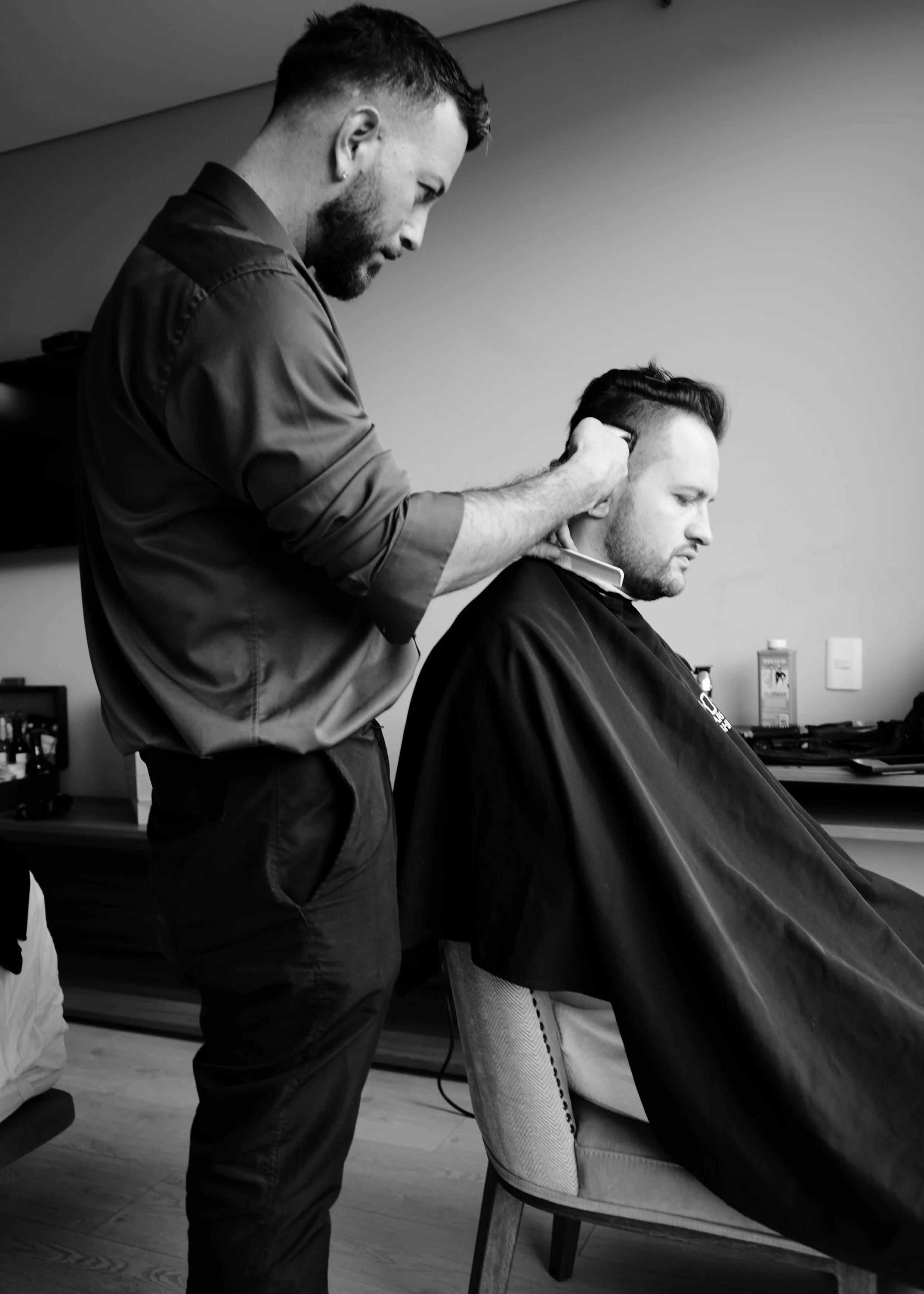 A barber cutting a man's hair in a barber shop. The barber is focused on his work, and the man is sitting comfortably in a chair draped with a cape.