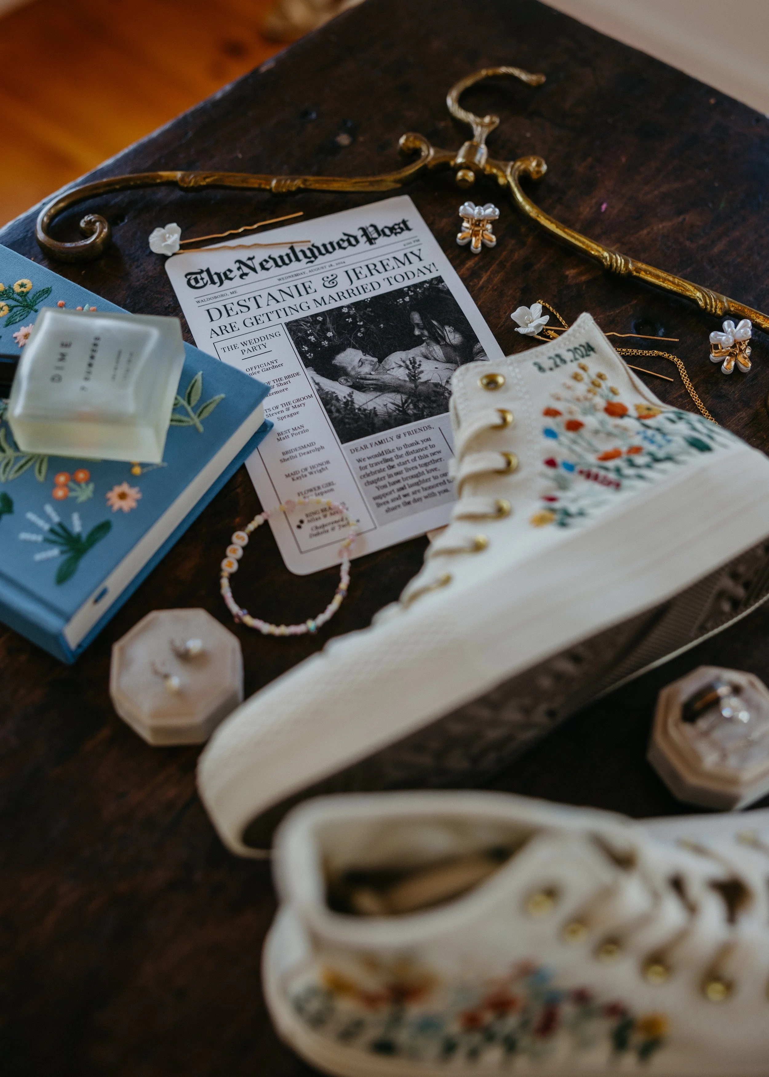 A wedding planning scene on a wooden surface featuring a wedding announcement, floral jewelry, and decorative items.