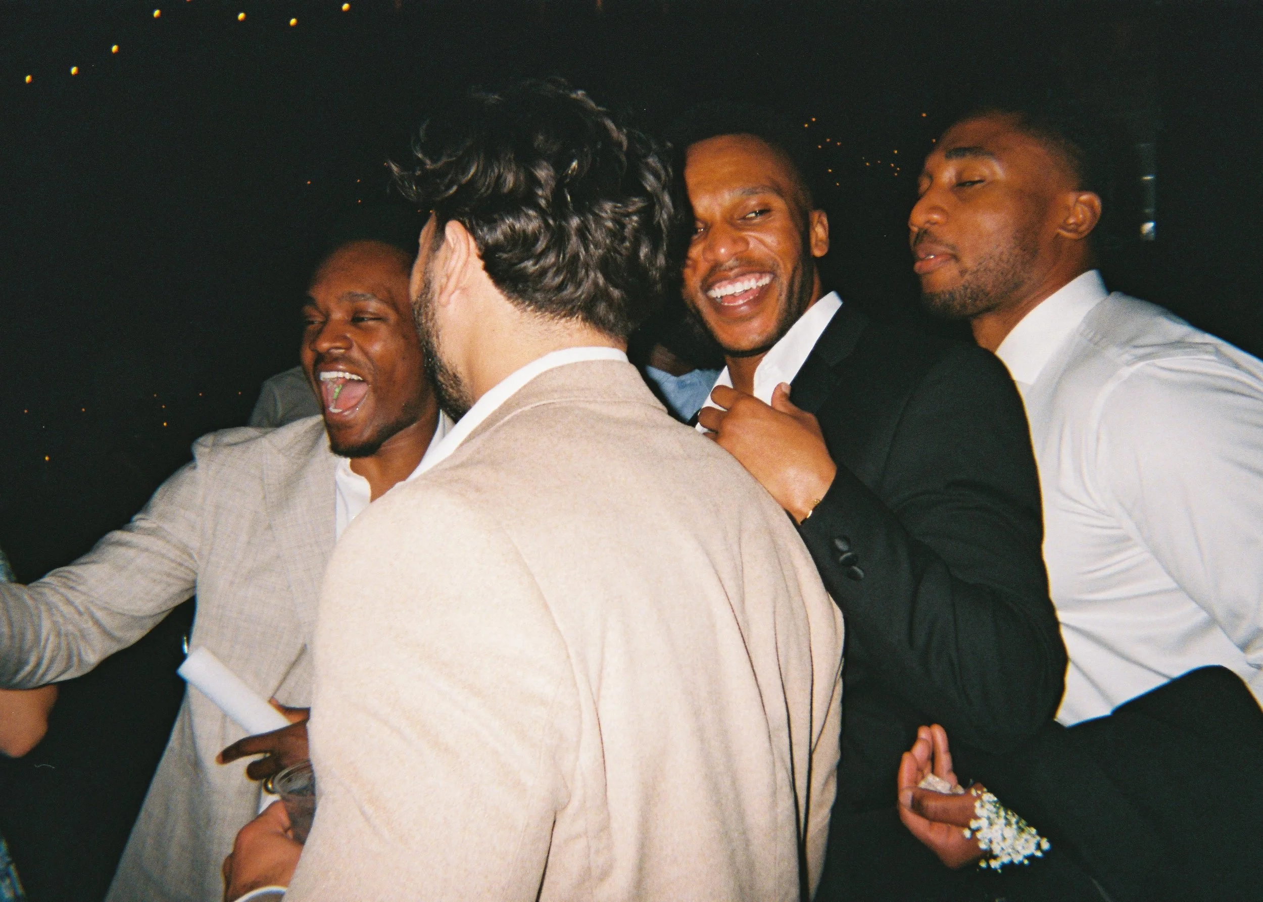 A group of people are at a social gathering, hugging and smiling. The scene appears to be joyful and friendly.