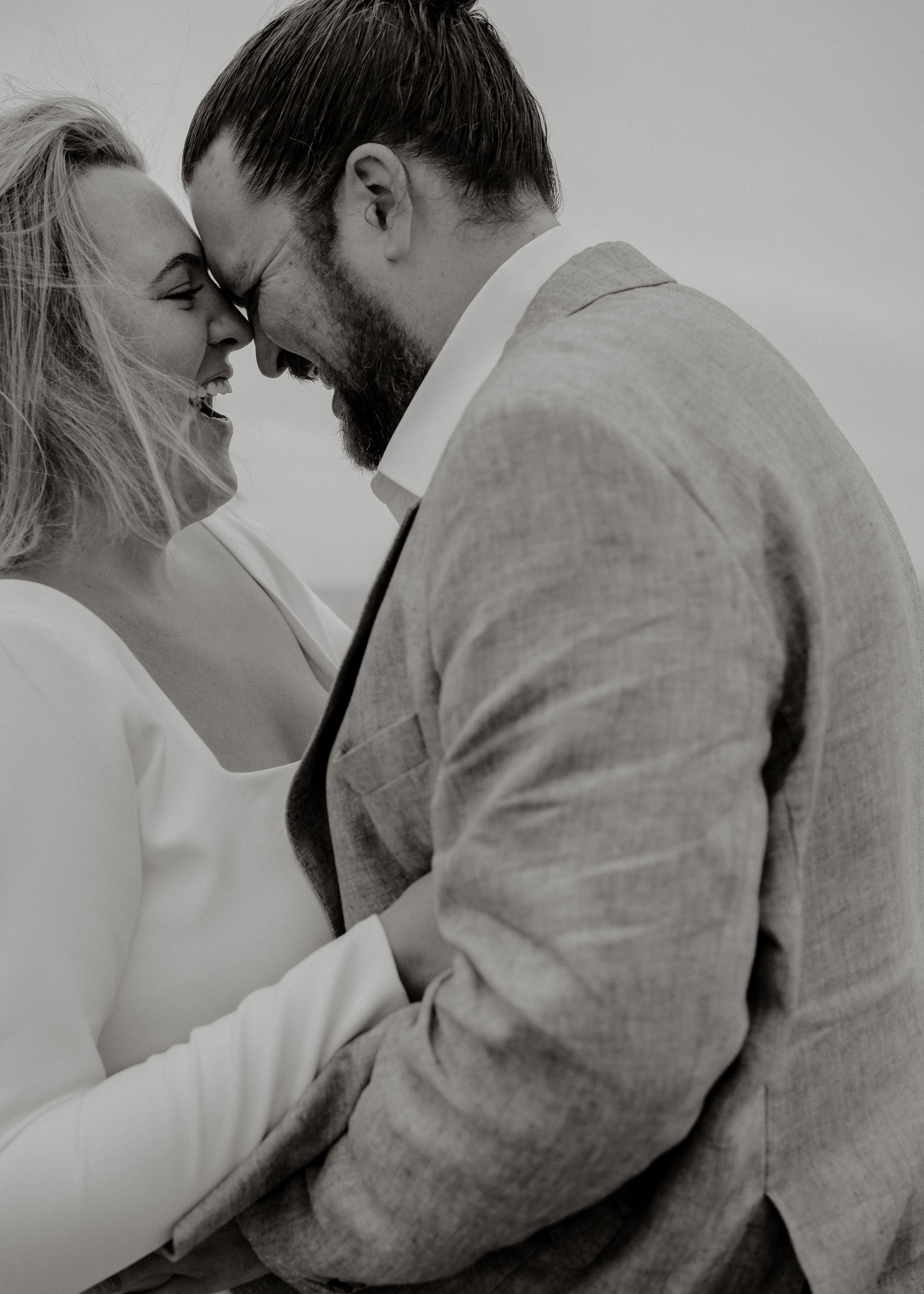 A black and white photo of a man and woman with their foreheads touching and eyes closed, smiling.