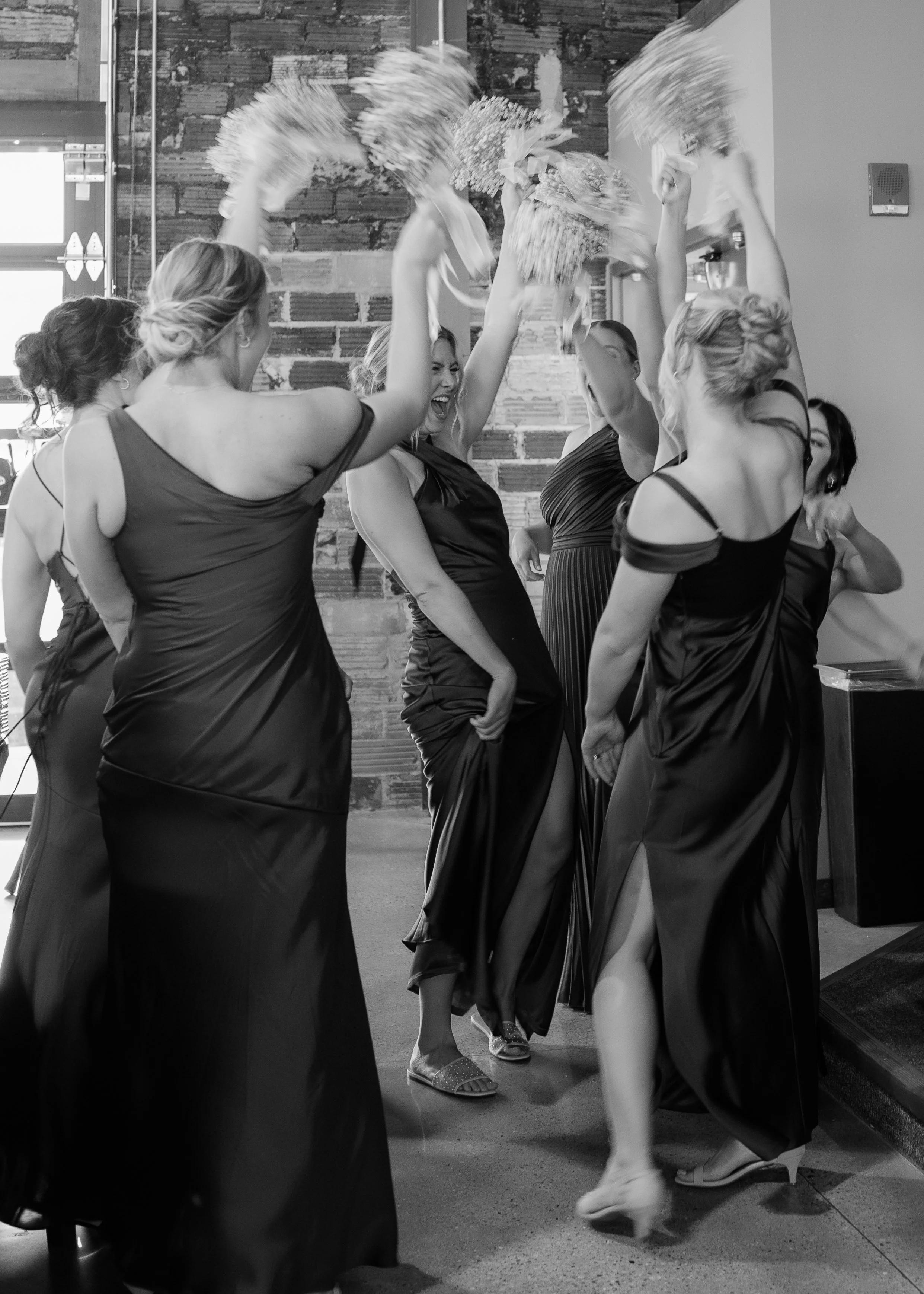 Women in formal dresses celebrating at a wedding reception, throwing flower bouquets into the air.