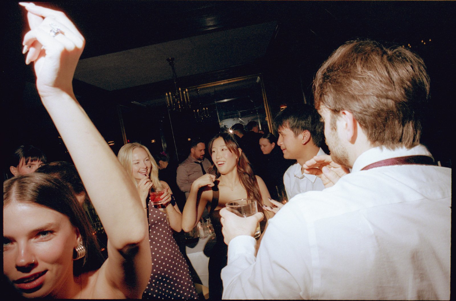 People dancing and socializing at a party with drinks in hand, in a dimly lit room.