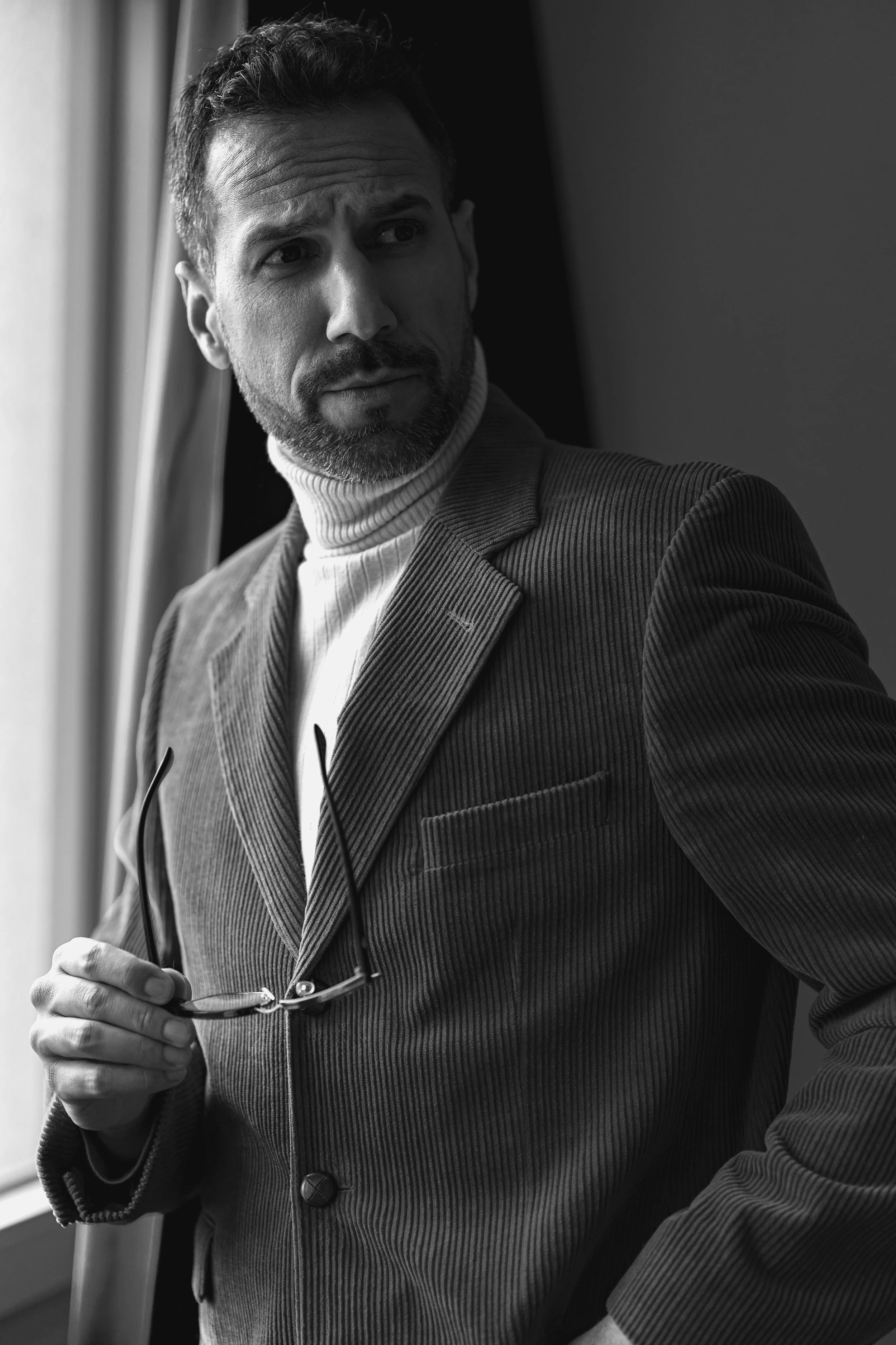 Schwarz-Weiß Businessportrait Frankfurt – Mann hält Brille, blickt nach draußen. Zeitloses Männerportrait, authentische Businessfotografie mit künstlerischer Note.