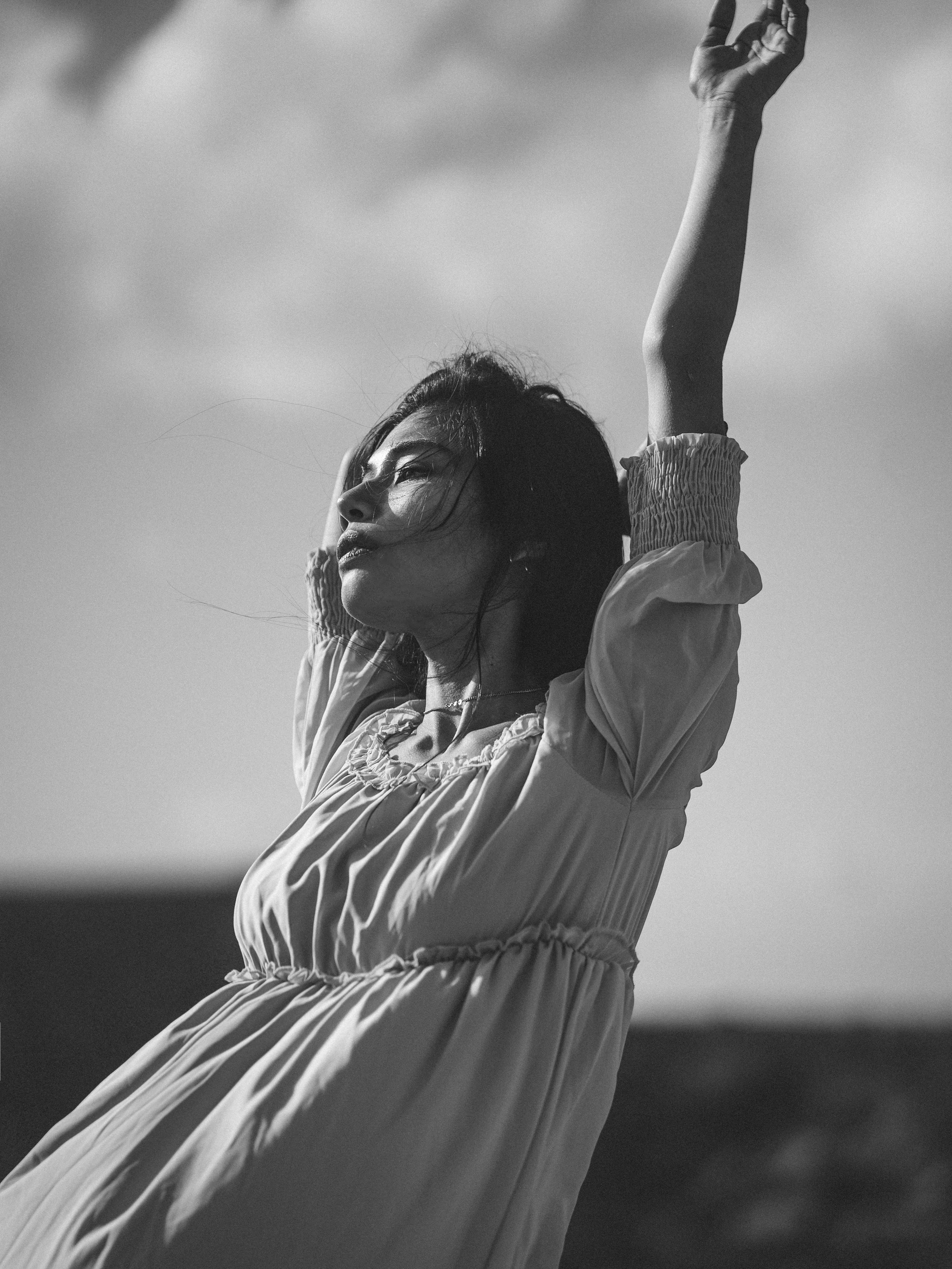 Künstlerische Schwarz-Weiß-Fotografie Wiesbaden – Frau mit erhobenen Armen, schaut in den Himmel, Wolken im Hintergrund. Ausdrucksstarkes Portrait mit moderner Bildsprache.