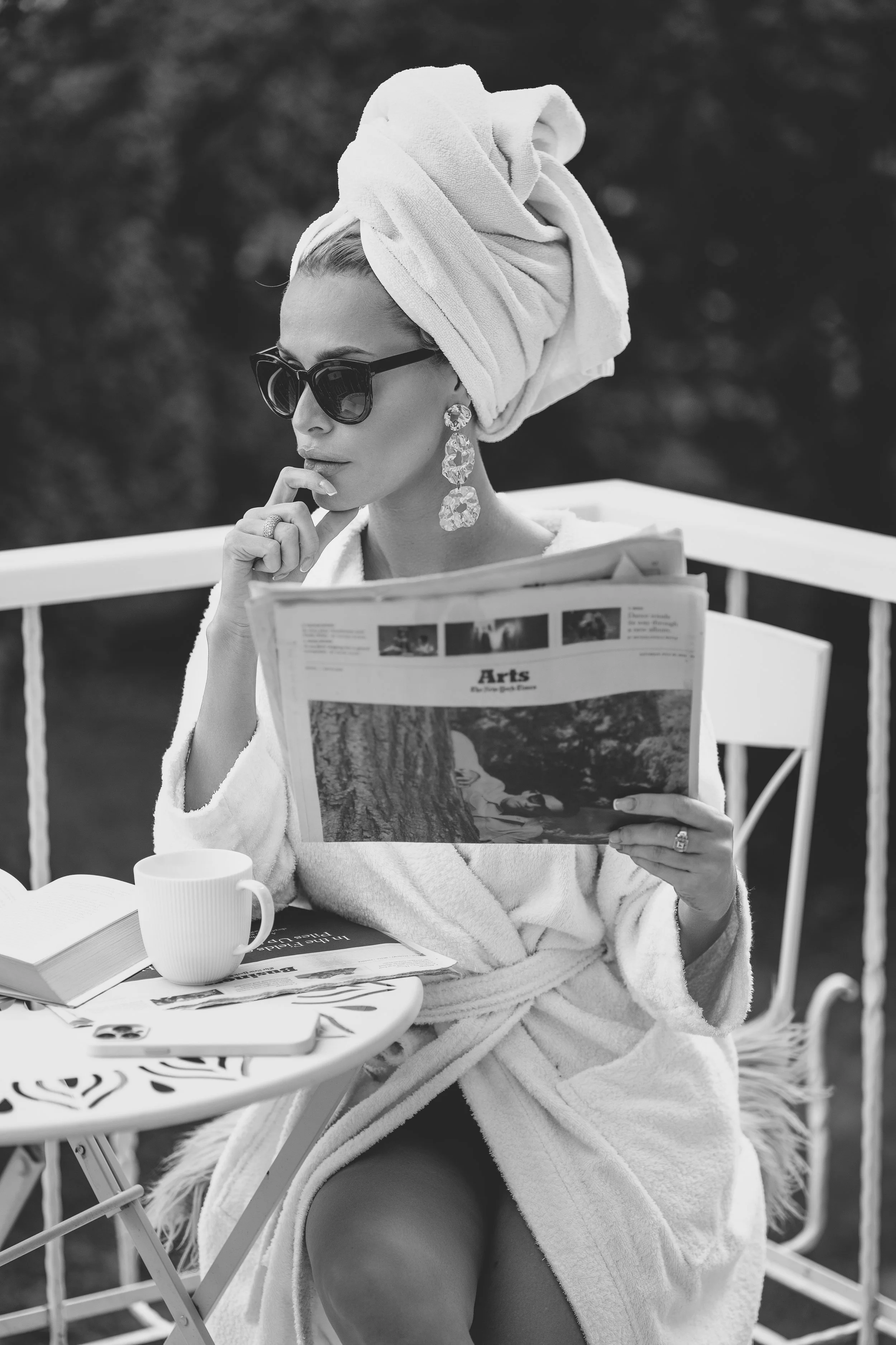 Lifestyle Schwarz-Weiß-Portrait Wiesbaden – Frau mit Turban, Sonnenbrille, Ohrringen, Bademantel, liest Zeitung auf Terrasse. Urbanes Frauenportrait mit modischem Touch und entspannter Atmosphäre.