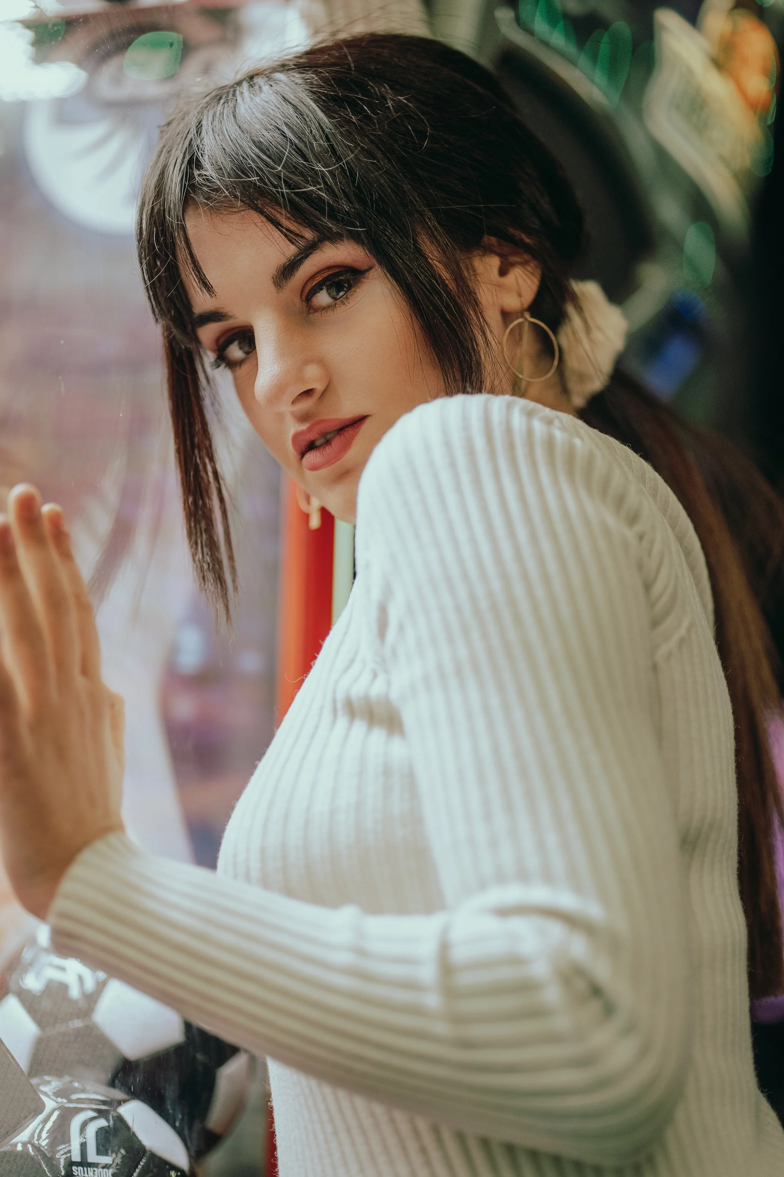 oderne Frauenfotografie Frankfurt – Junge Frau mit dunklen Haaren, rotem Lippenstift, weißer Pullover, steht vor Fensterwand in Eiscafé. Urbanes Portrait mit modernem Look und natürlichem Licht.