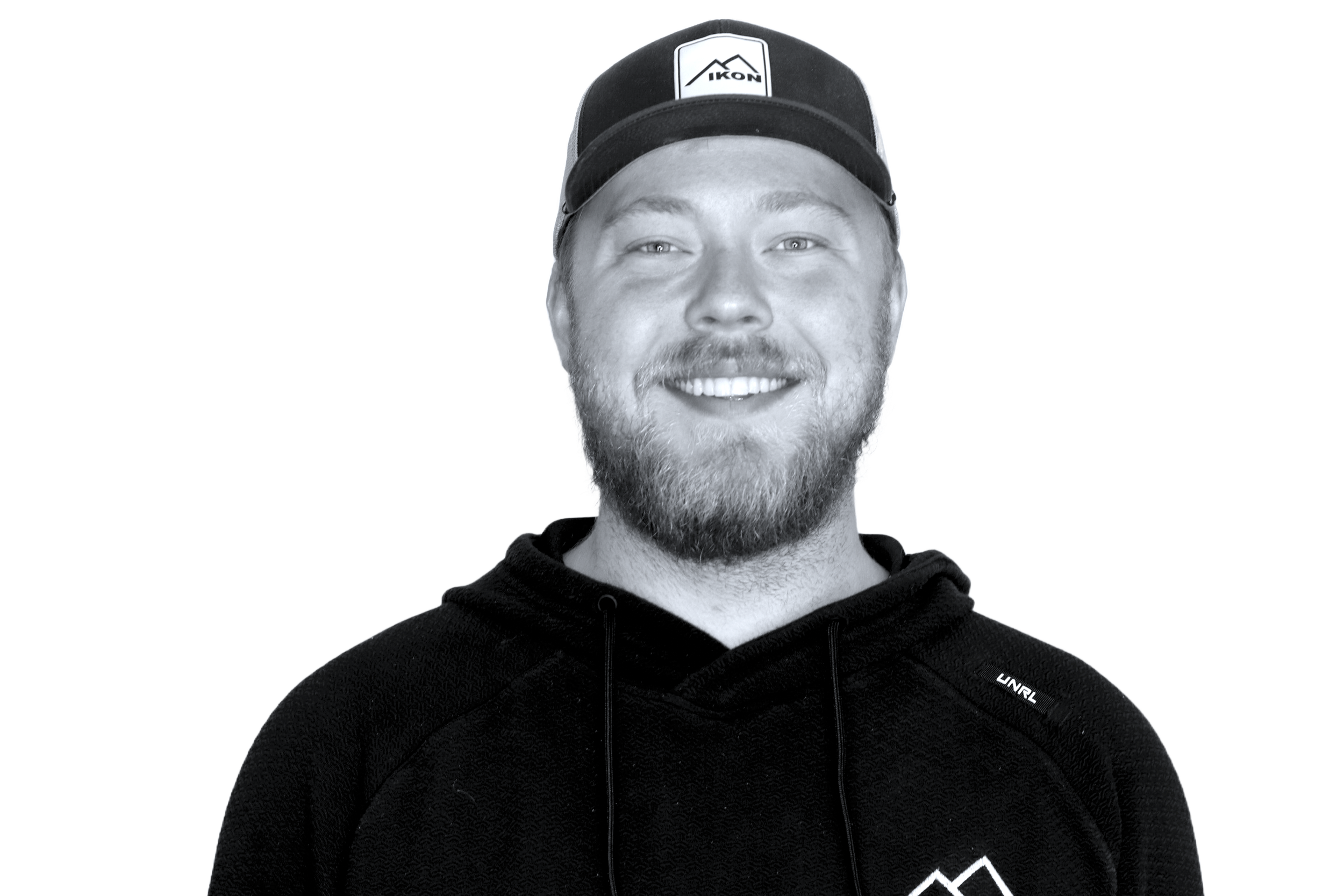 A smiling person wearing a baseball cap with the word 'IKON' and a hoodie, in a black and white photo.