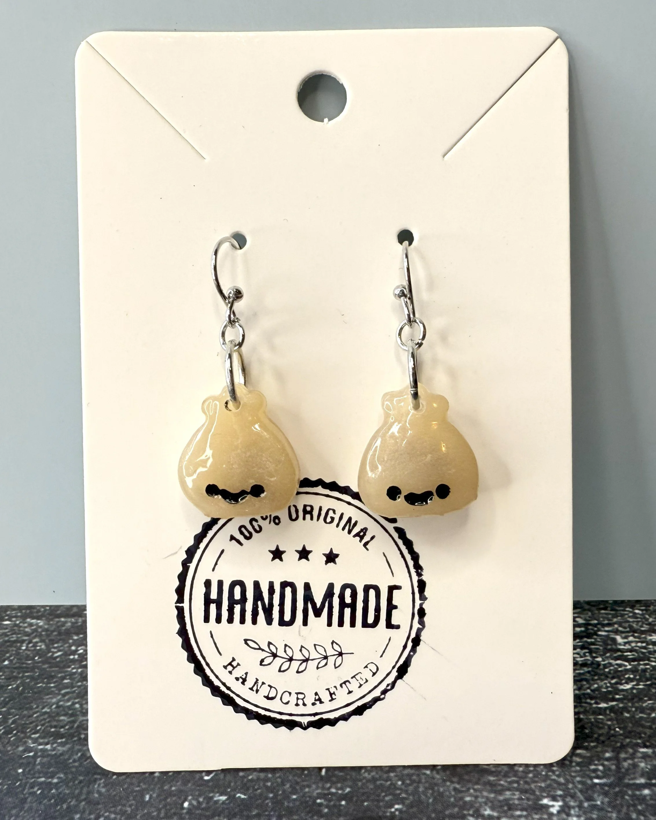 Tiny dumplings, big personality. Each handmade earring features a smiling dumpling with a translucent clay pouch — hold them to the light to see the “filling” inside! Available with different smile colors (because even dumplings have moods), they’re