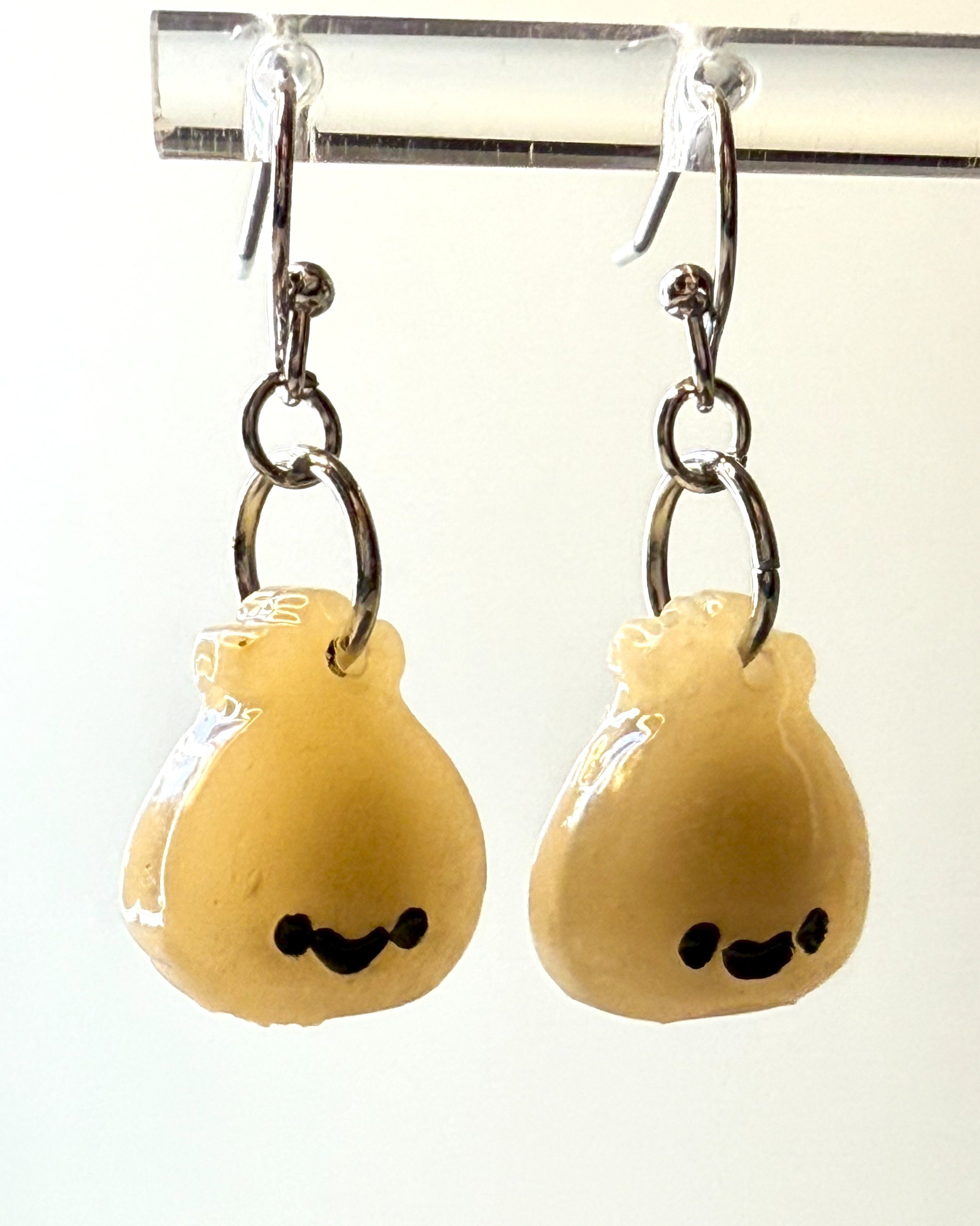 Cute smiley face dumpling earrings made from polymer clay, shown hanging from a metal earring stand for display, with a softly lit background