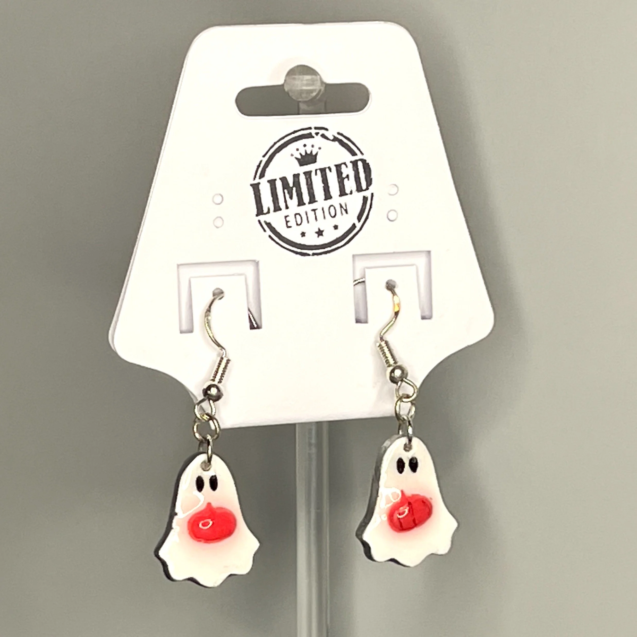 White ghost earrings featuring deep red pumpkins, shown on a branded display card on a marble background