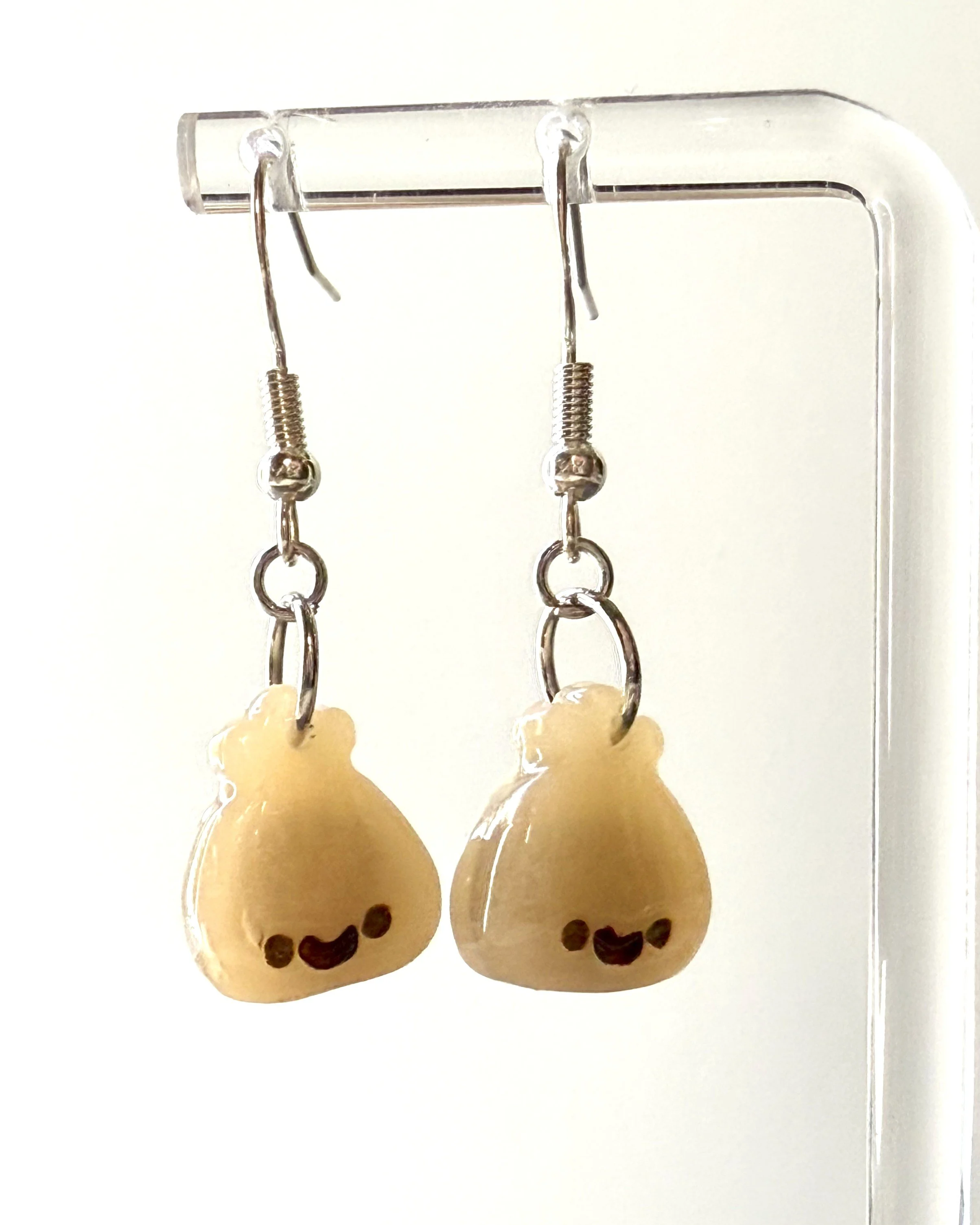 Cute smiley face dumpling earrings made from polymer clay, shown hanging from a metal earring stand for display, with a softly lit background