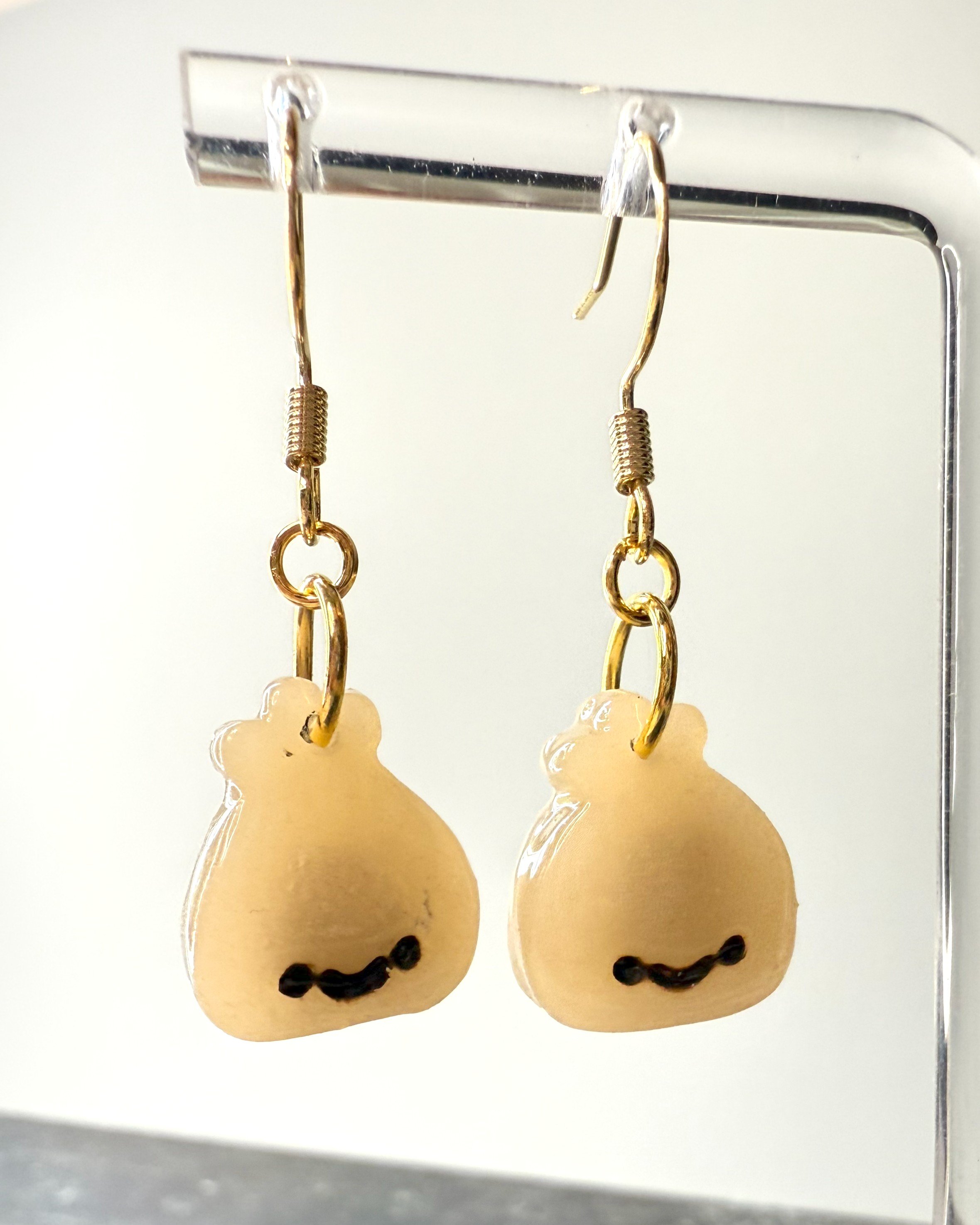 Cute smiley face dumpling earrings made from polymer clay, shown hanging from a metal earring stand for display, with a softly lit background