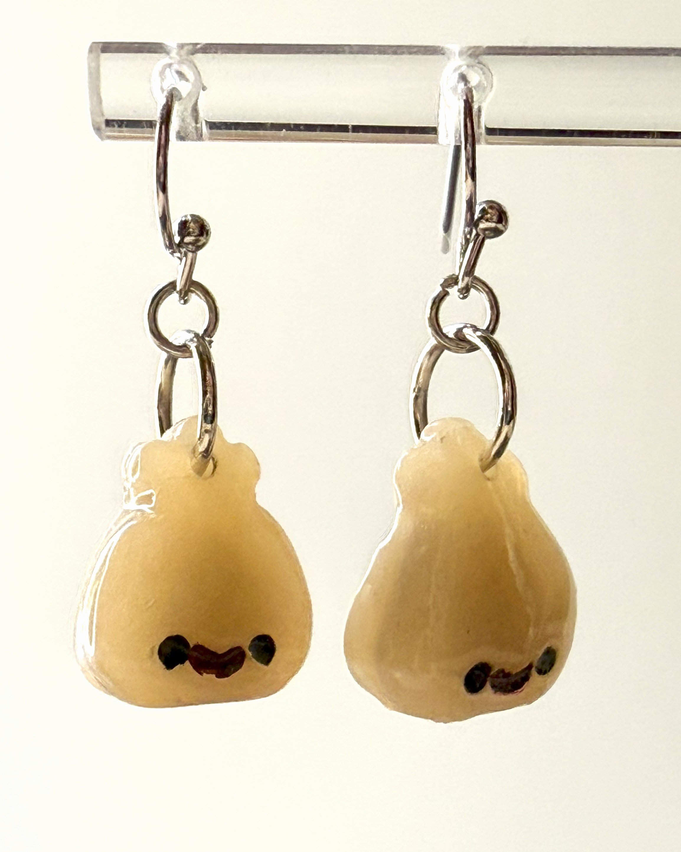Cute smiley face dumpling earrings made from polymer clay, shown hanging from a metal earring stand for display, with a softly lit background
