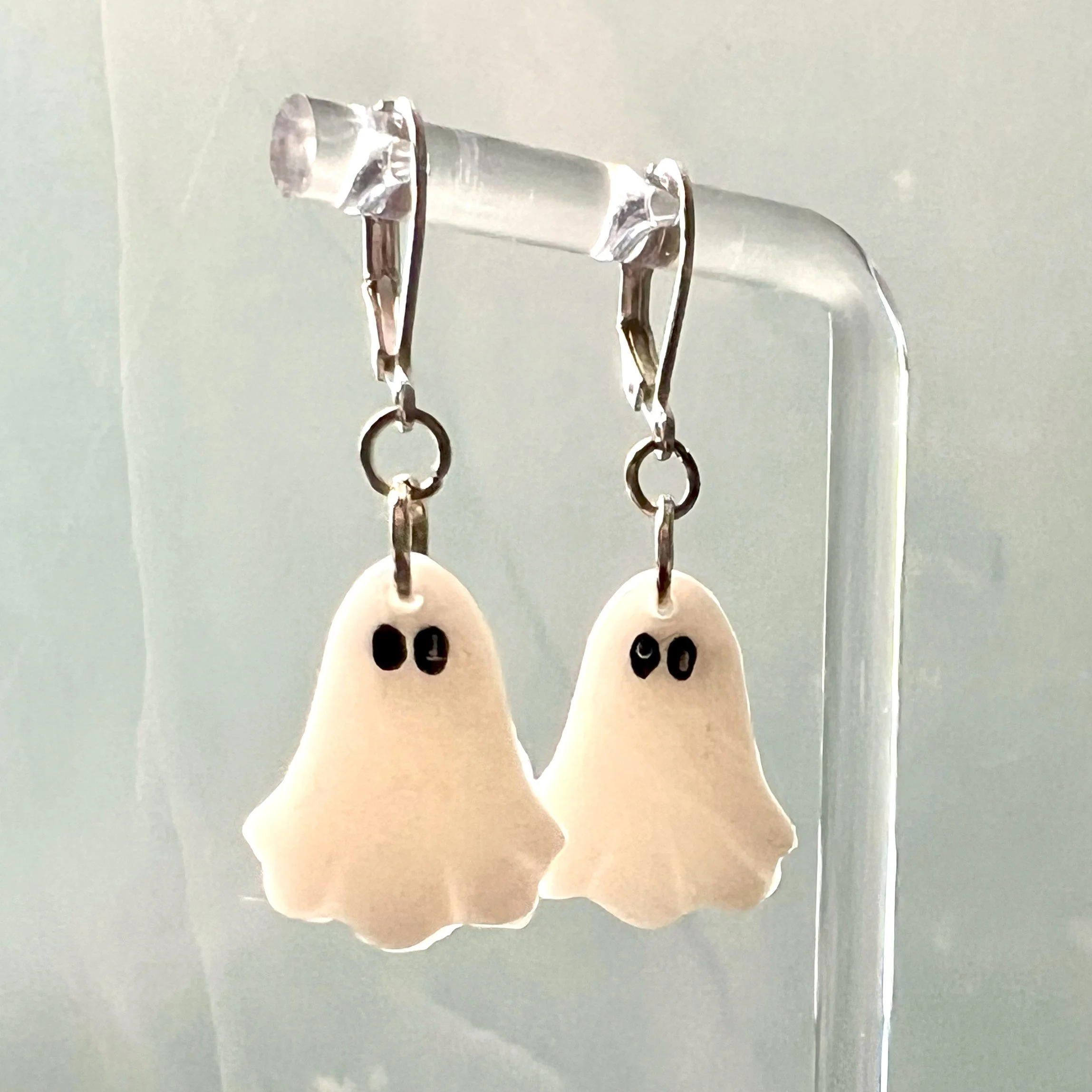 Minimalist translucent ghost earrings without pumpkins, hanging on earring stand for display against a marble-patterned background