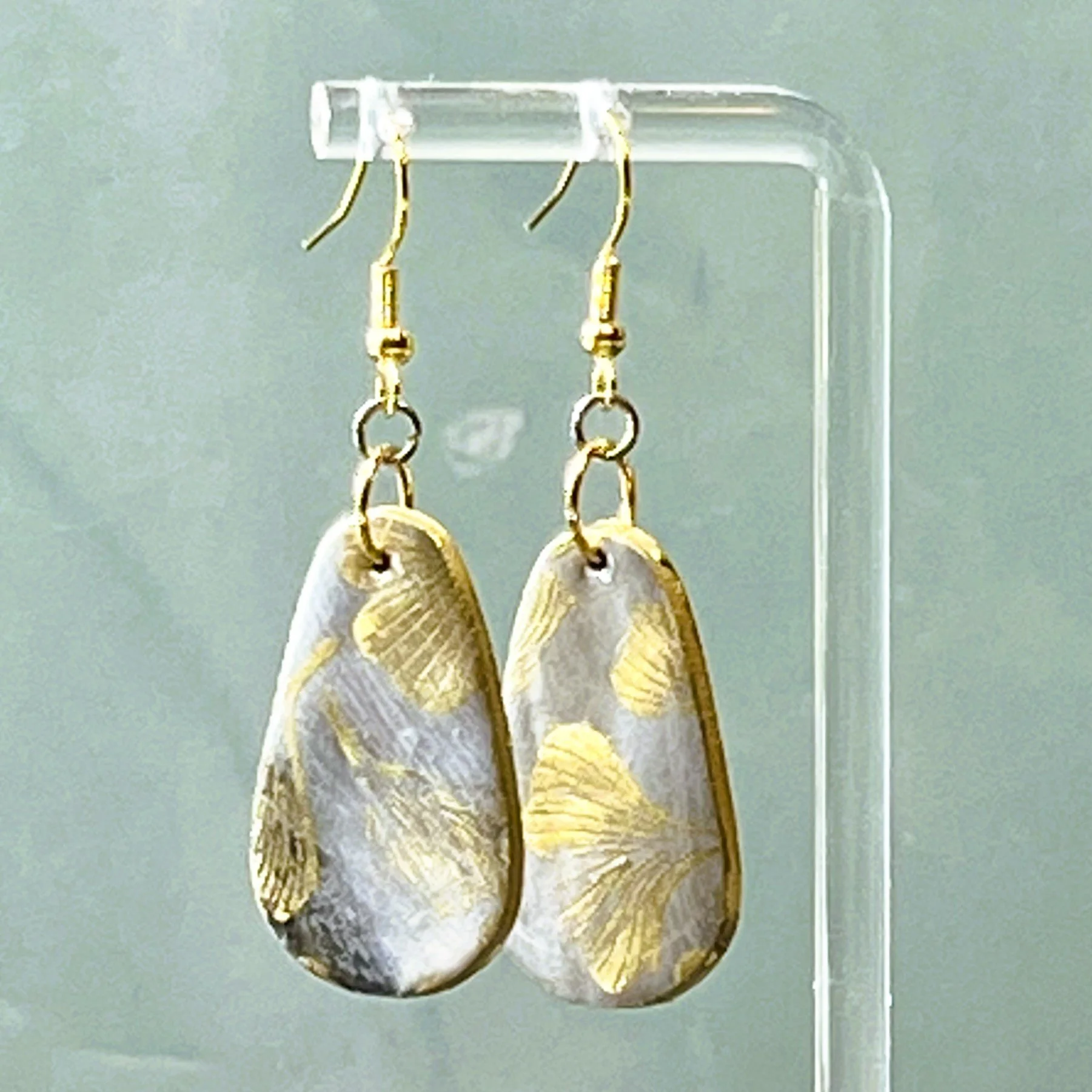 Earrings are a pair of polymer clay faux stone dangle earrings resembling a black, grey, white marbled stone with gold print ginkgo biloba leaf pattern