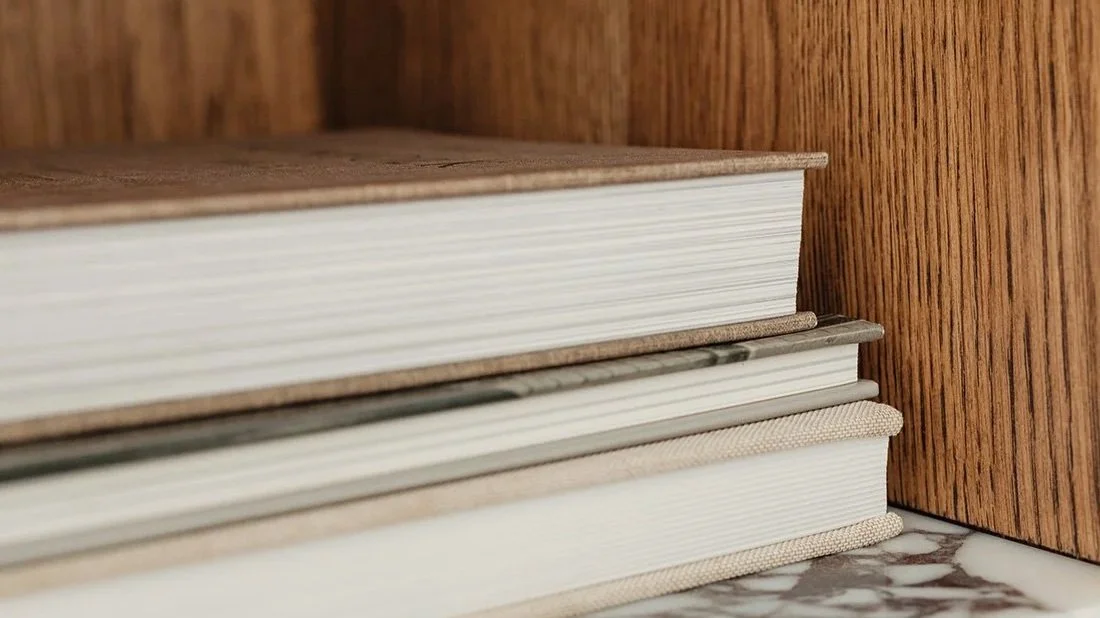 Stacked books on a wooden shelf with a marble base.