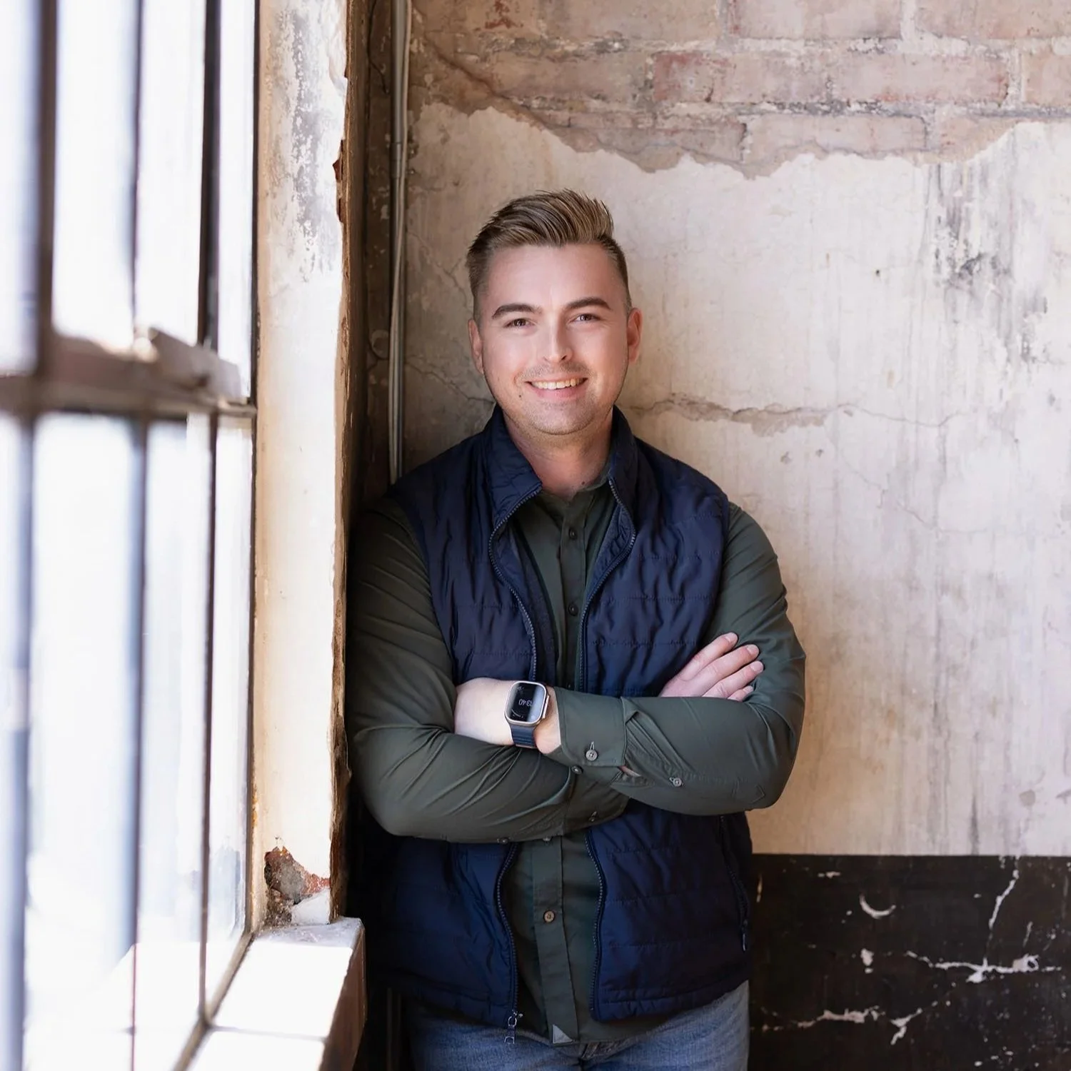 Alex M. Roberts, Ph.D., standing by a window with arms crossed in a warm, natural-light office setting, psychologist specializing in psychological testing.