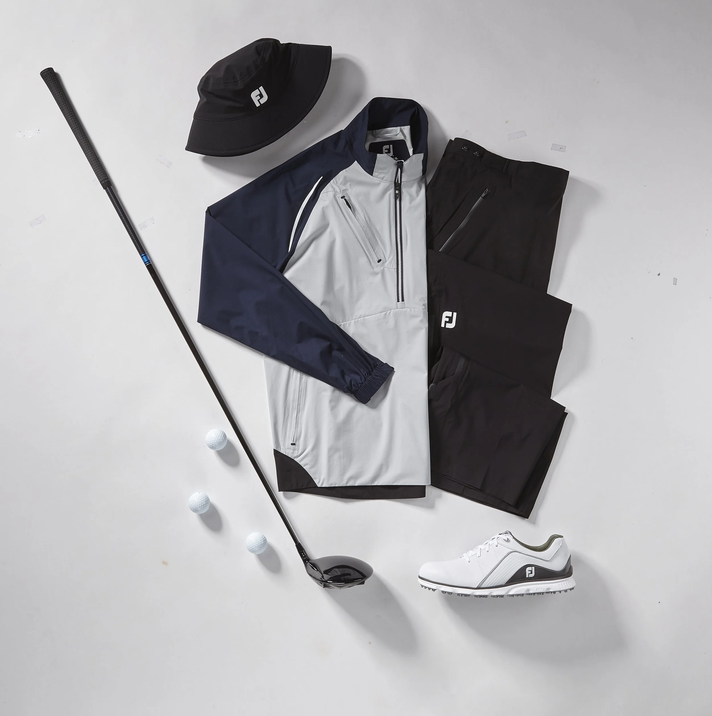 Golf clothing and equipment including a black golf cap, navy and white golf jacket, black golf pants, white golf shoes, a golf club, and three golf balls arranged on a white background.