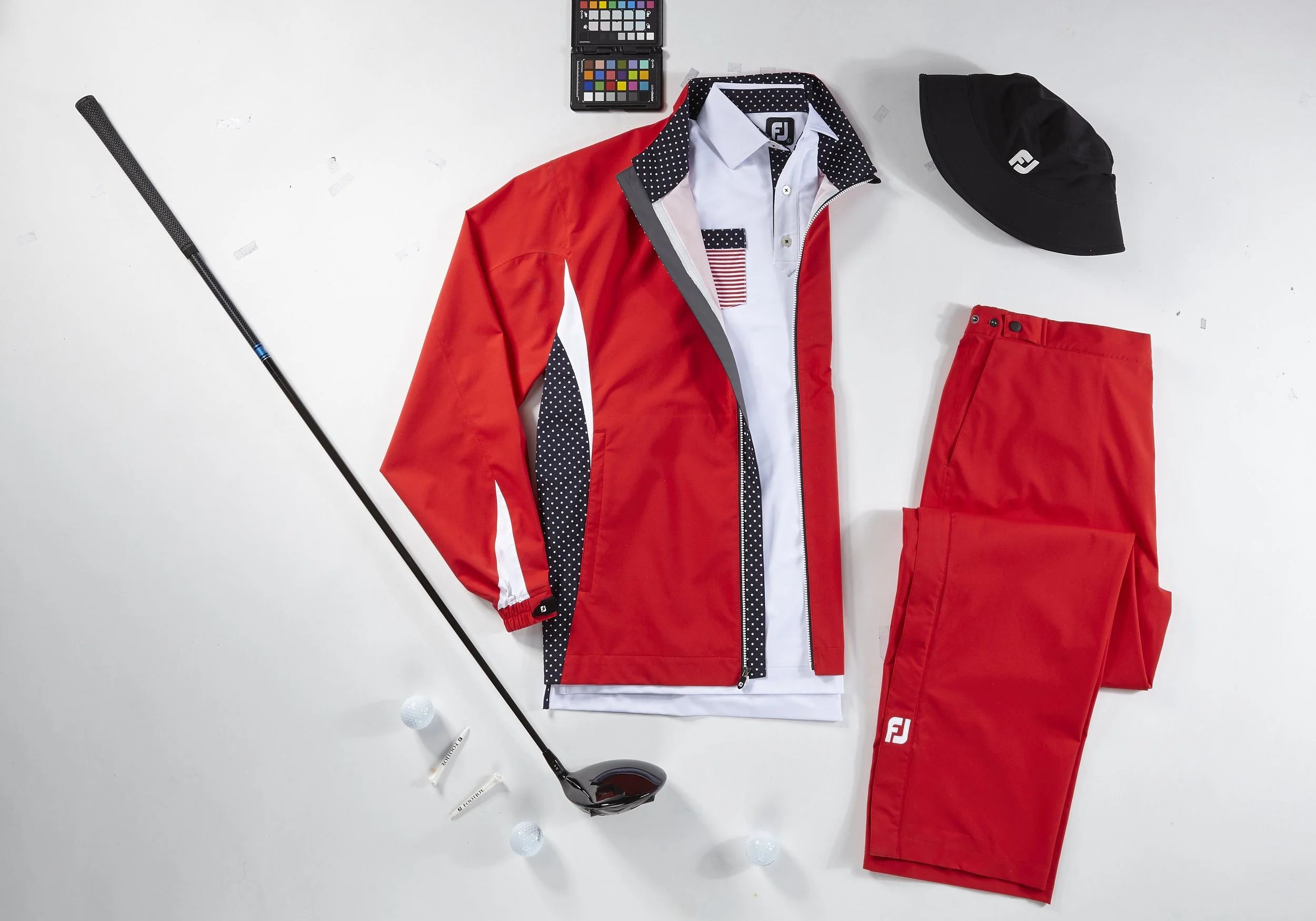 Golf attire including a red jacket with navy polka dot accents, white shirt with American flag patch, red pants with FJ logo, black cap, golf clubs, golf balls, tees, and color calibration chart on a white background.