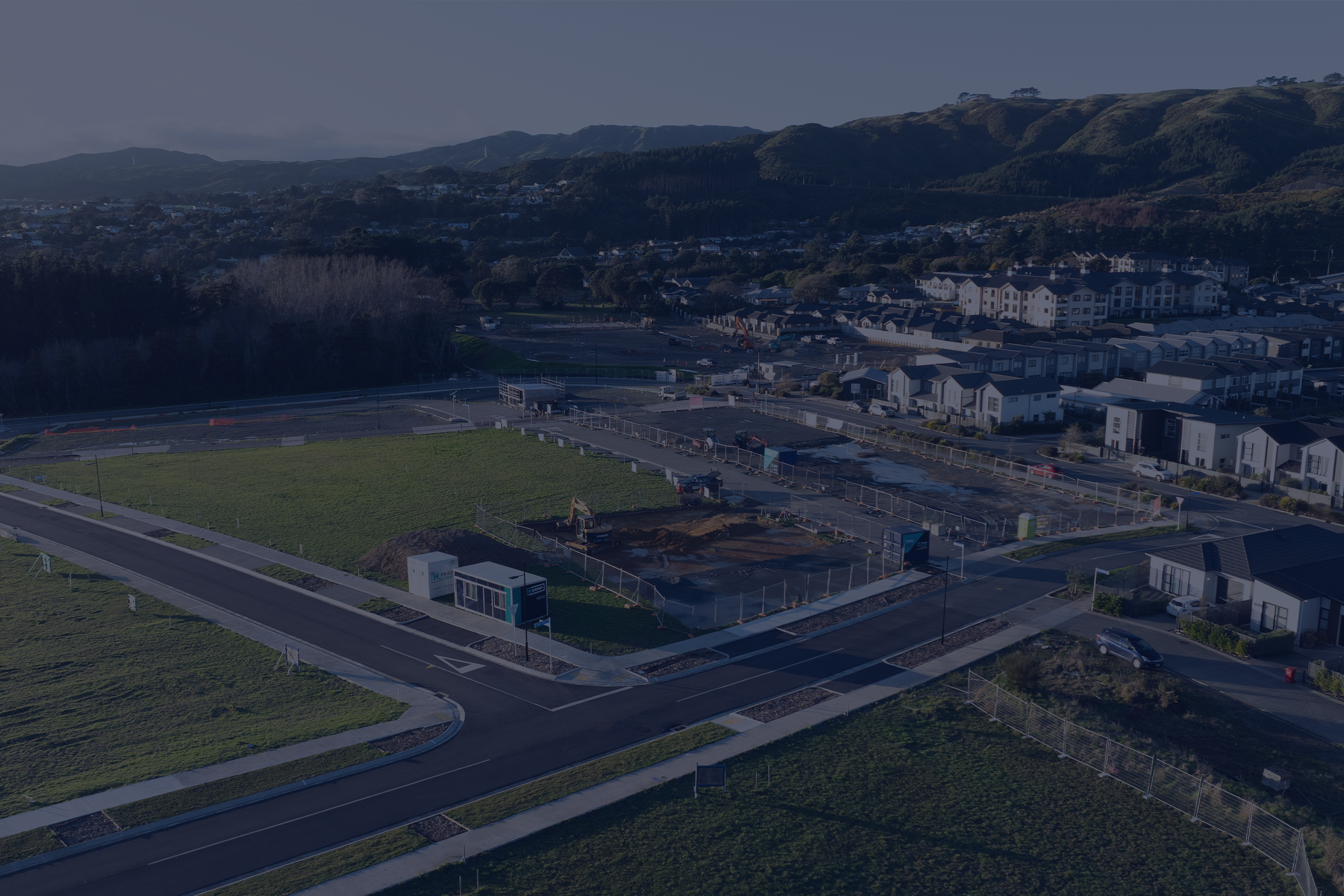 A residential neighborhood with construction site and green hills in the background.