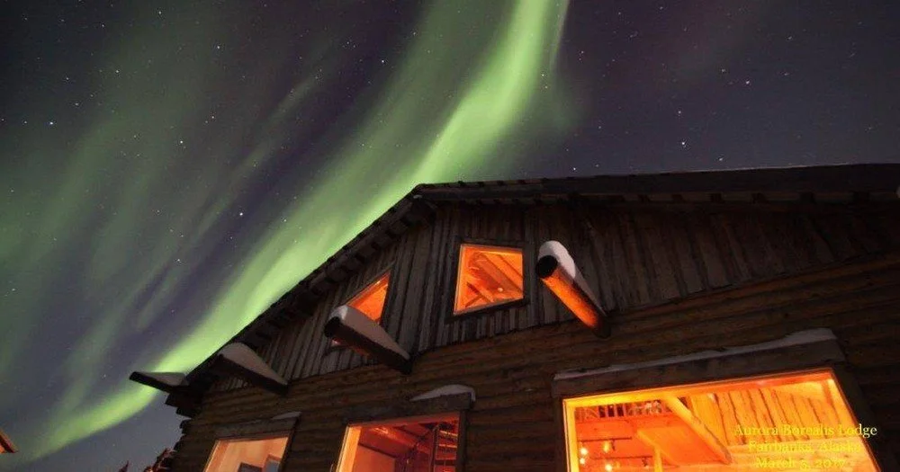 Green Aurora Borealis lights dancing in the night sky above the warmly lit Aurora Borealis Lodge near Fairbanks, Alaska.