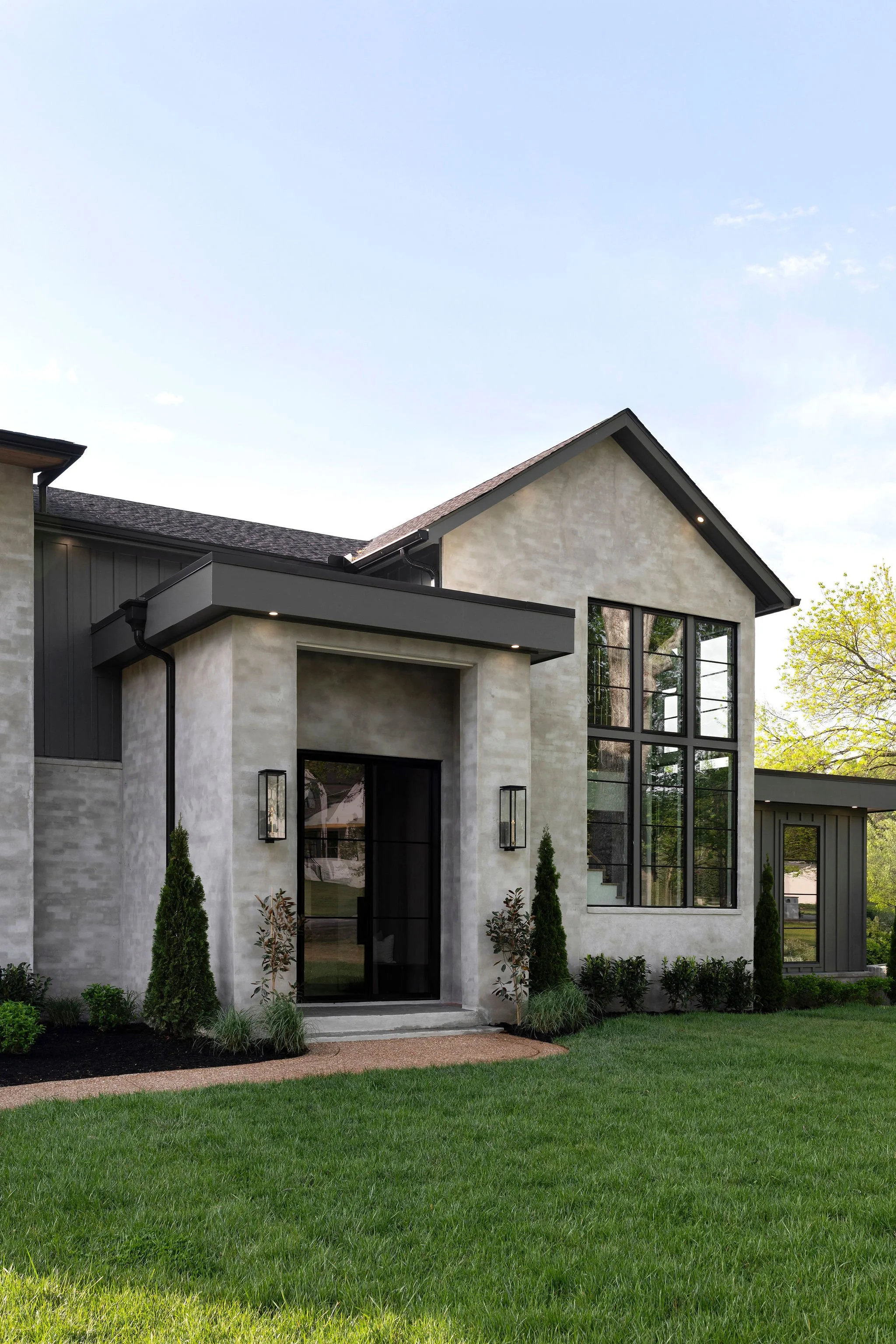 Modern house with large windows, landscaped yard, and green lawn during daytime.