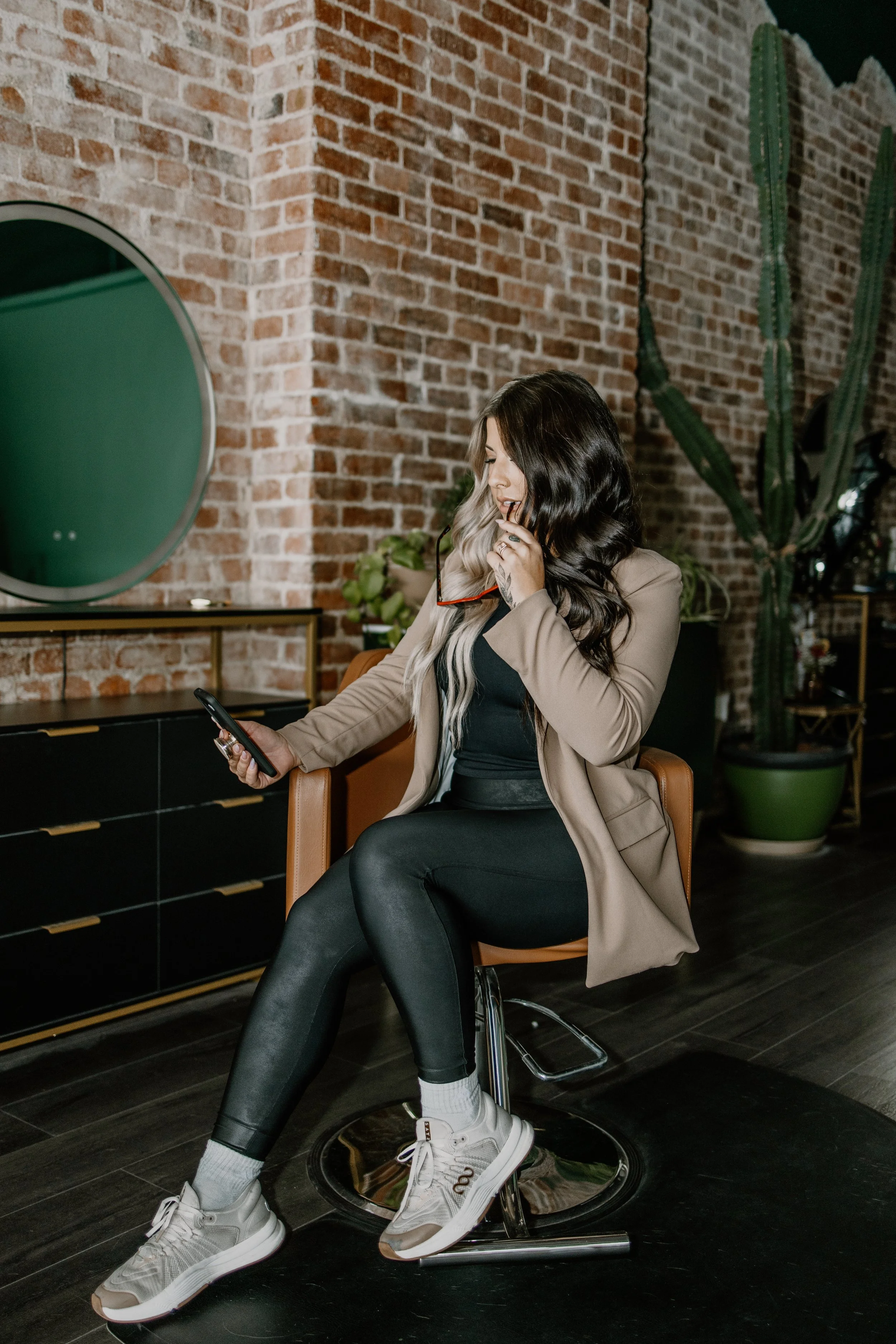 Pittsburgh hair extension artist poses in a salon chair holding a phone and sunglasses