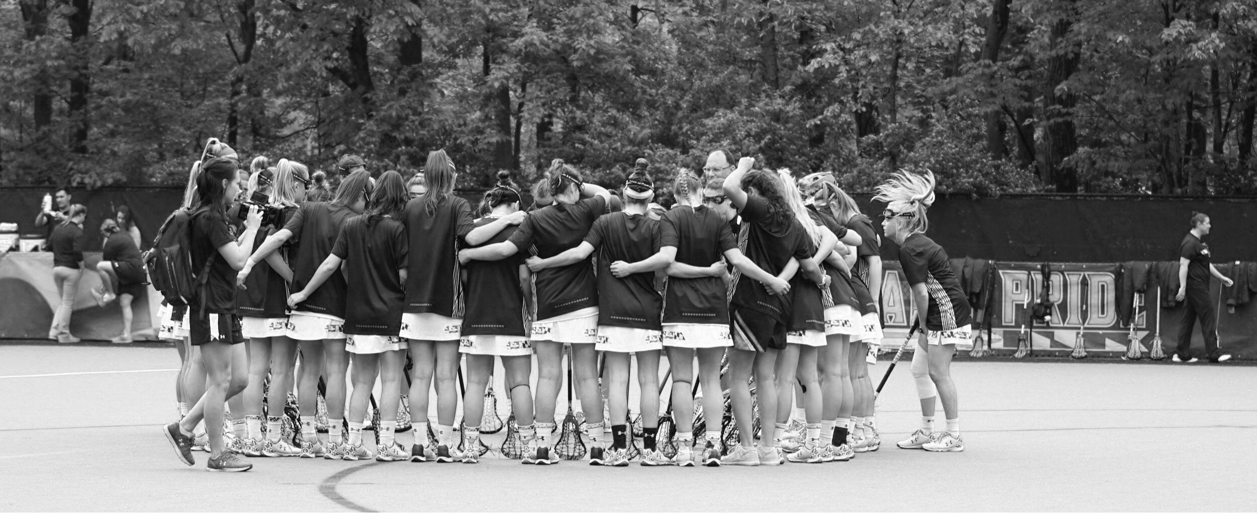 A man with a beard and short hair is pointing at a whiteboard with a diagram on it during a presentation in a classroom or conference room. The whiteboard has a blue diagram and text, and a person in the foreground is holding a water bottle.