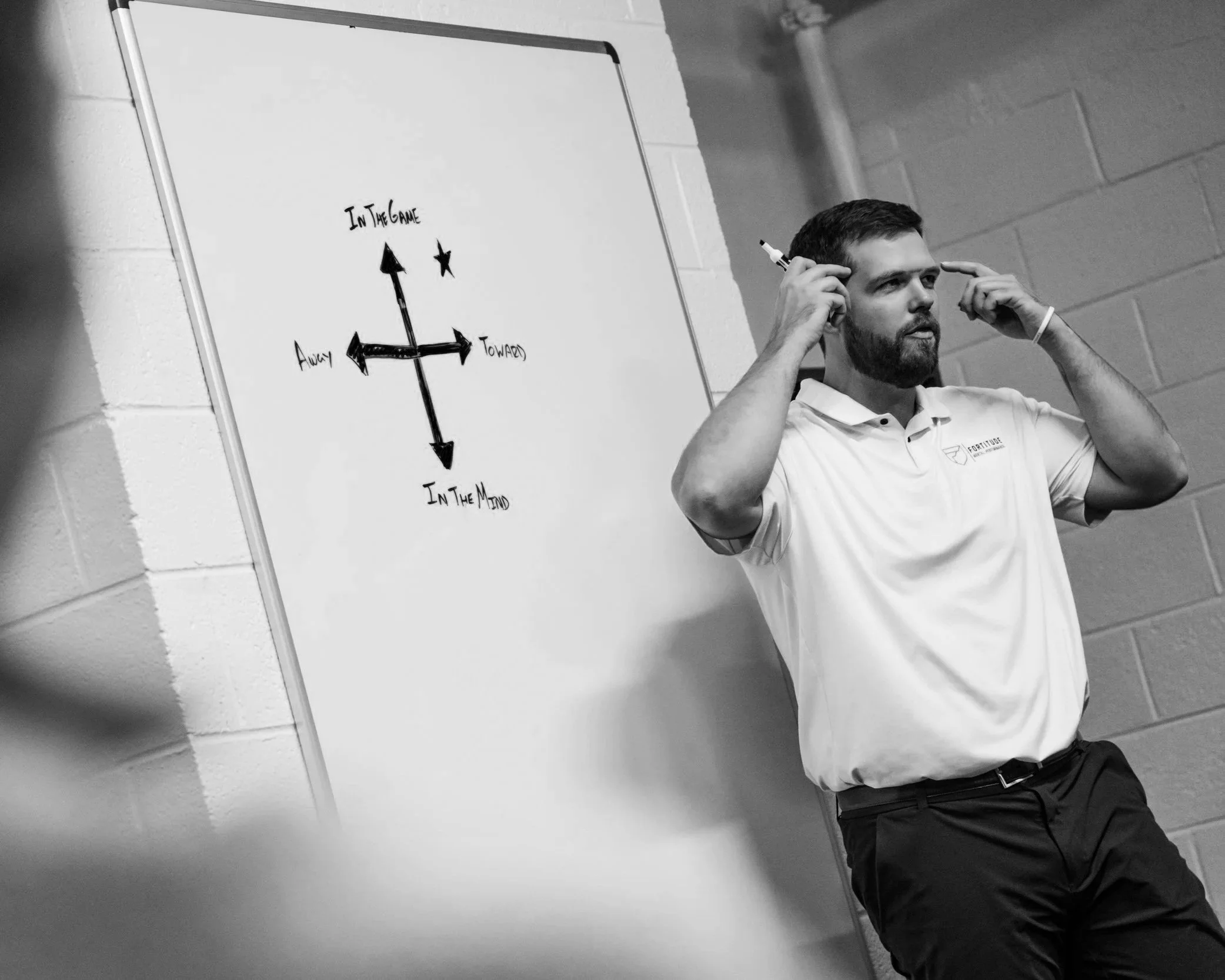 Two young men playing an electronic game on a table with colorful lights, while an adult watches. Other people observe in the background.