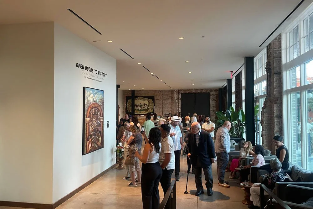 People visiting an art gallery or museum, observing paintings and artwork on the walls, with some sitting on benches and engaging with the exhibits.