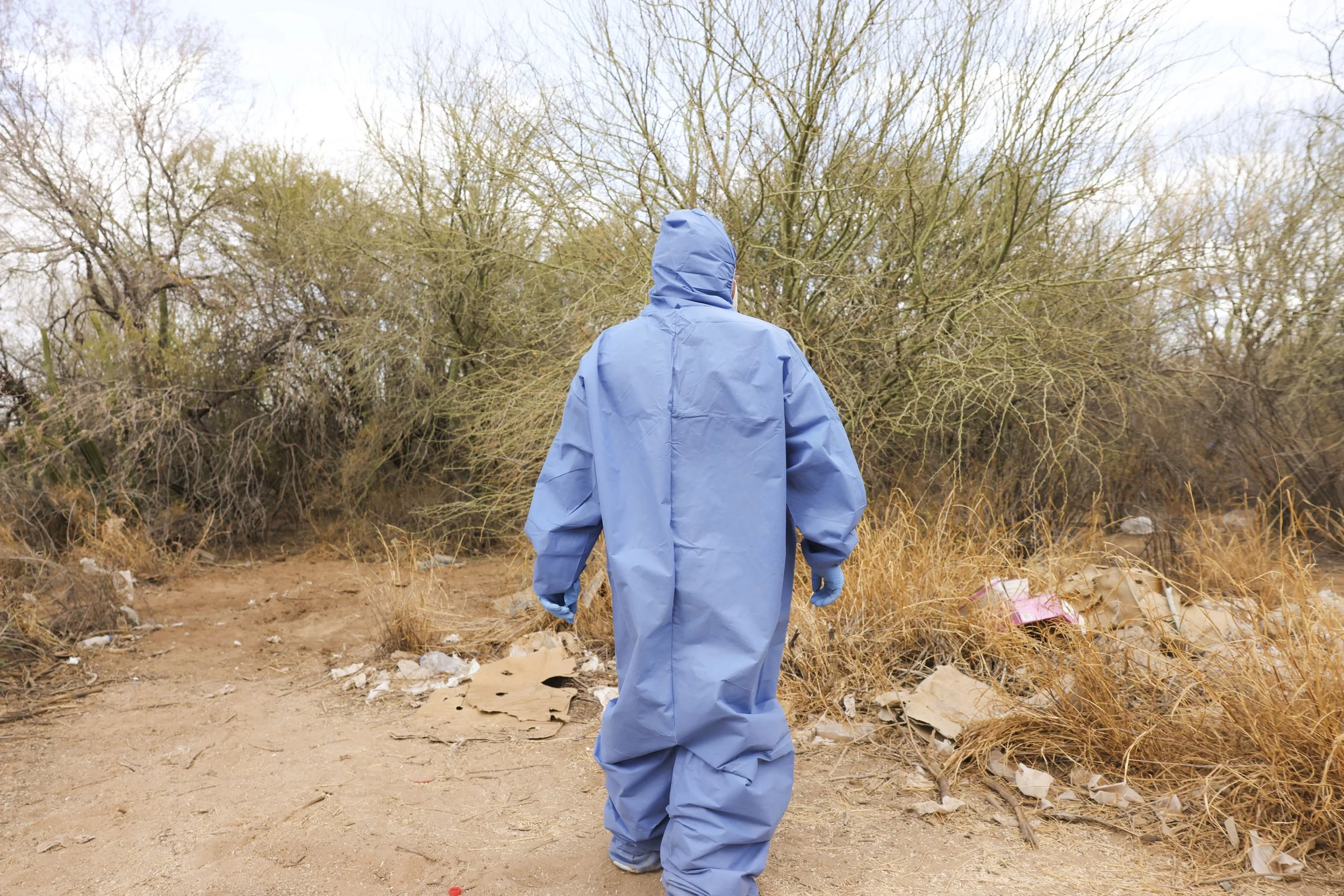 Forensic specialists in blue suits.
Working the scene in the dry desert.