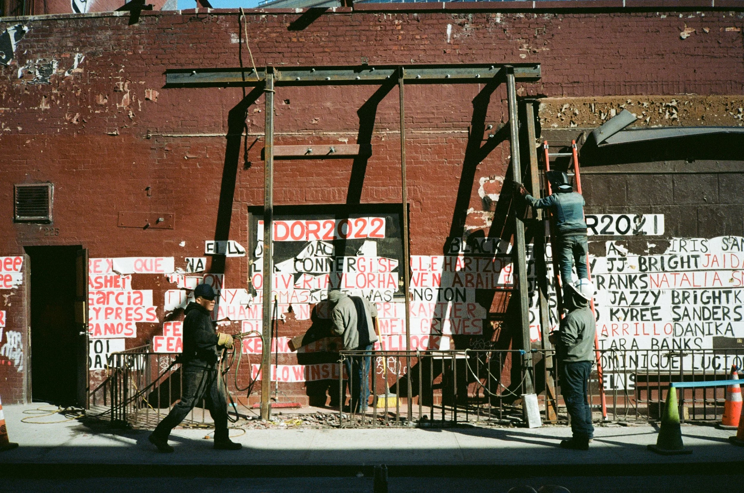 Workers installing campaign signs on a brick wall, with some signs saying "DOR 2022" and various candidate names.