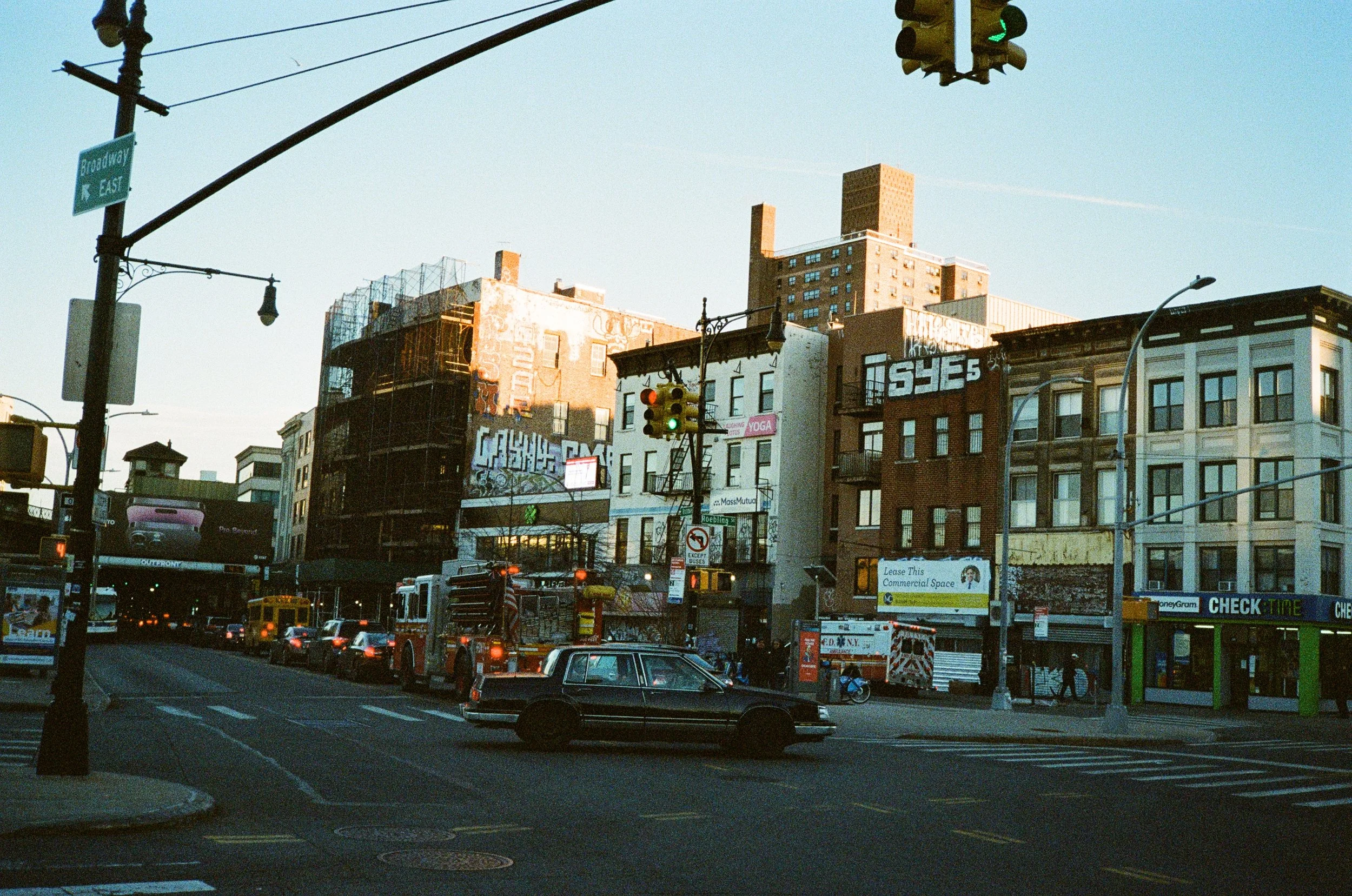 City street scene with buildings, traffic lights, cars, buses, and pedestrians in an urban area during daytime