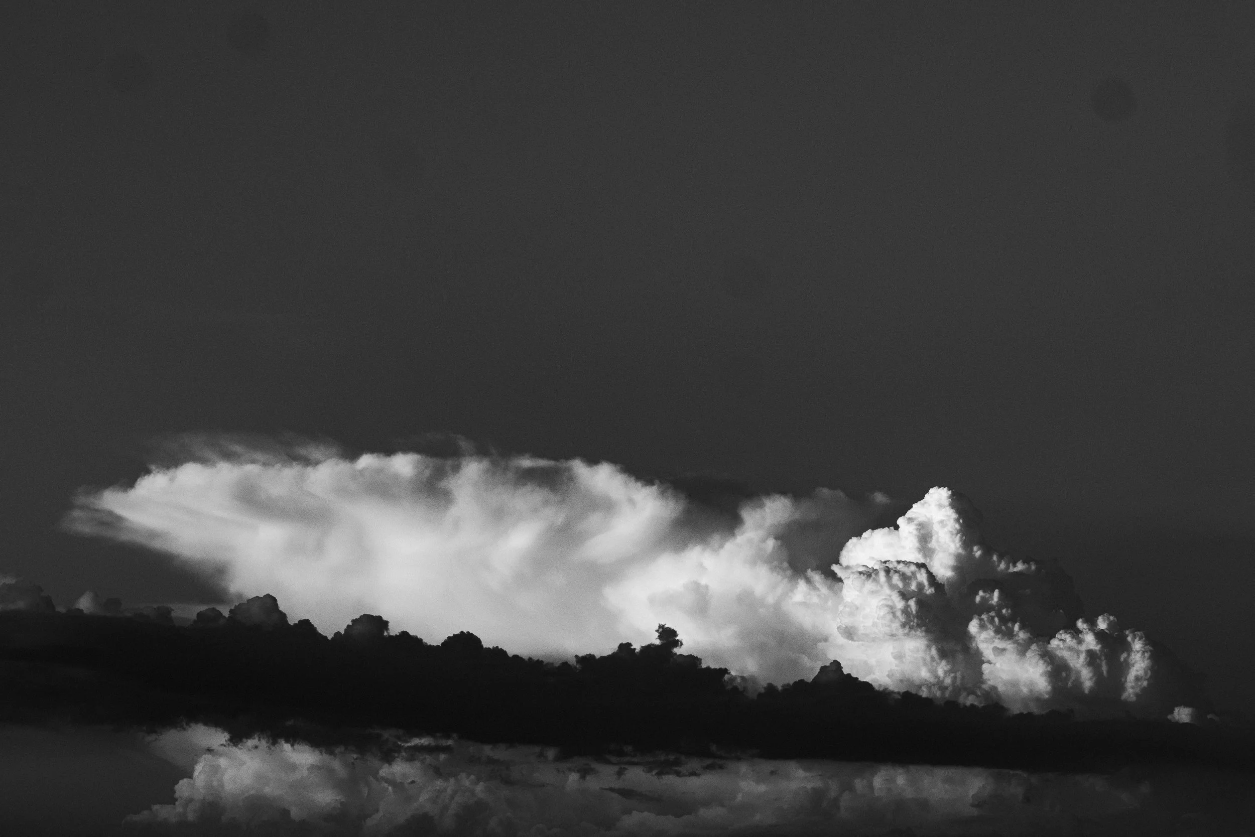 Black and white photo of cloud formations in the sky, with a dark horizon line.