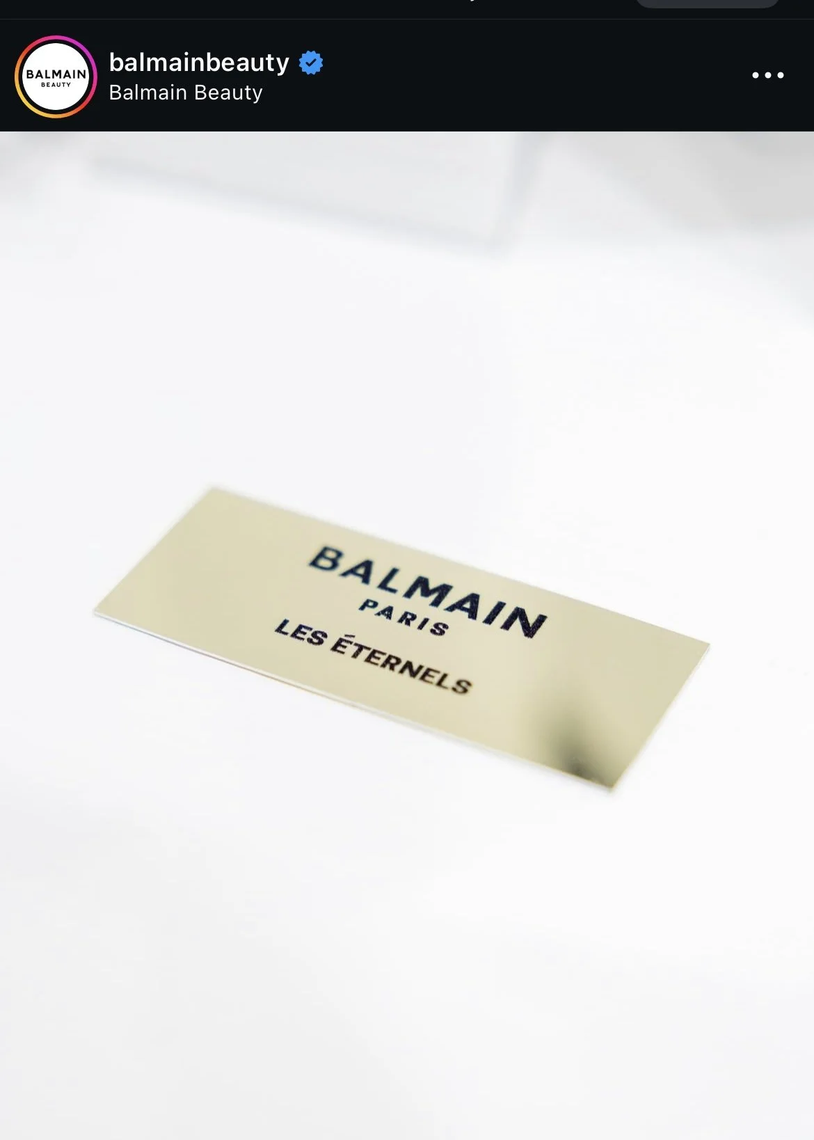 Close-up of a beige label with black text reading "BALMAIN PARIS LES ÉTERNELS" on a white surface.