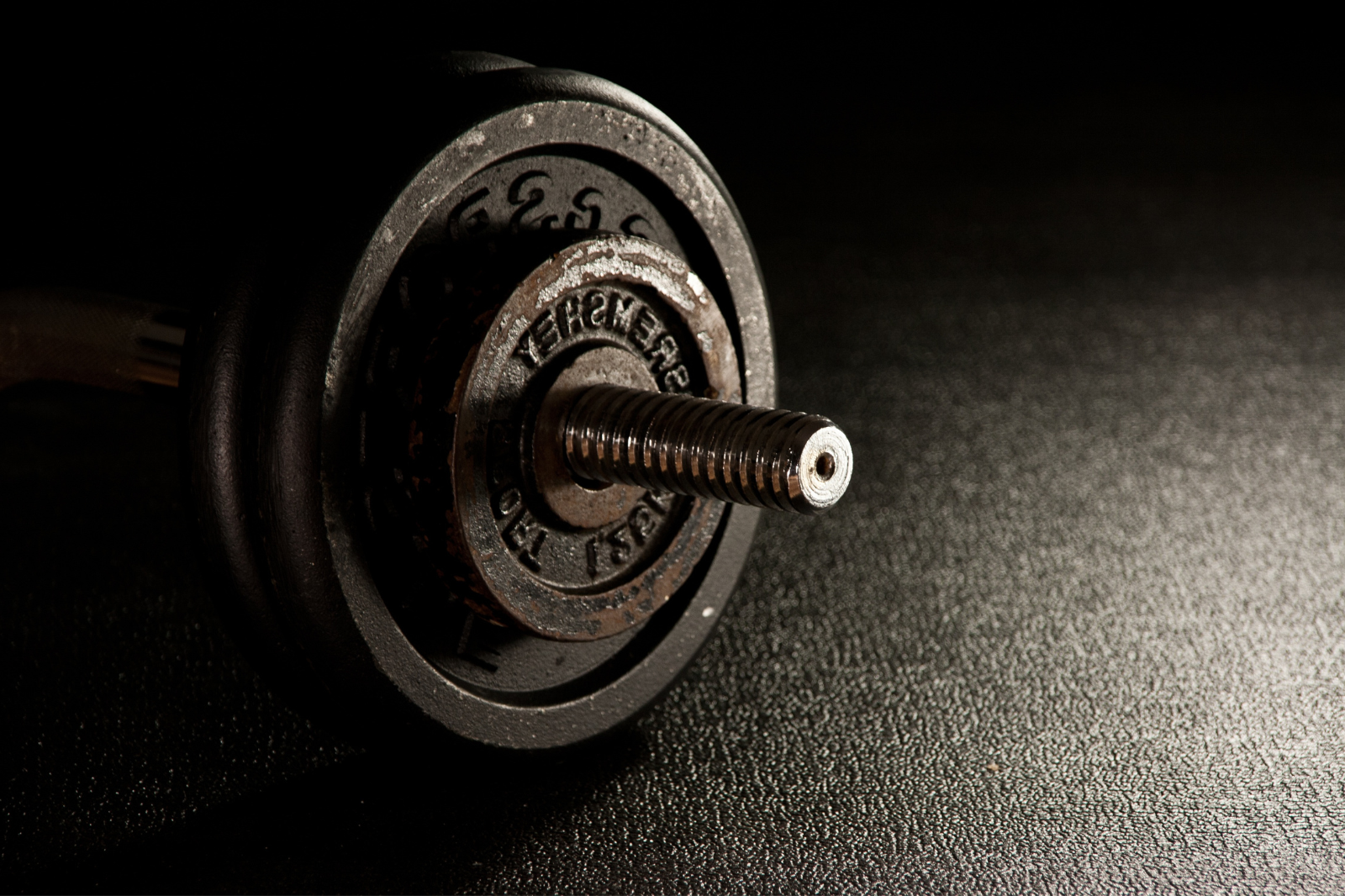 Close-up of a black weight with a metal threaded rod in front of a black textured surface.