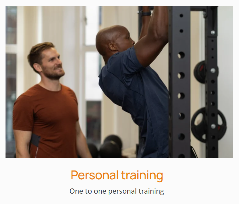 A person performing pull-ups in a gym while a trainer watches and encourages him.